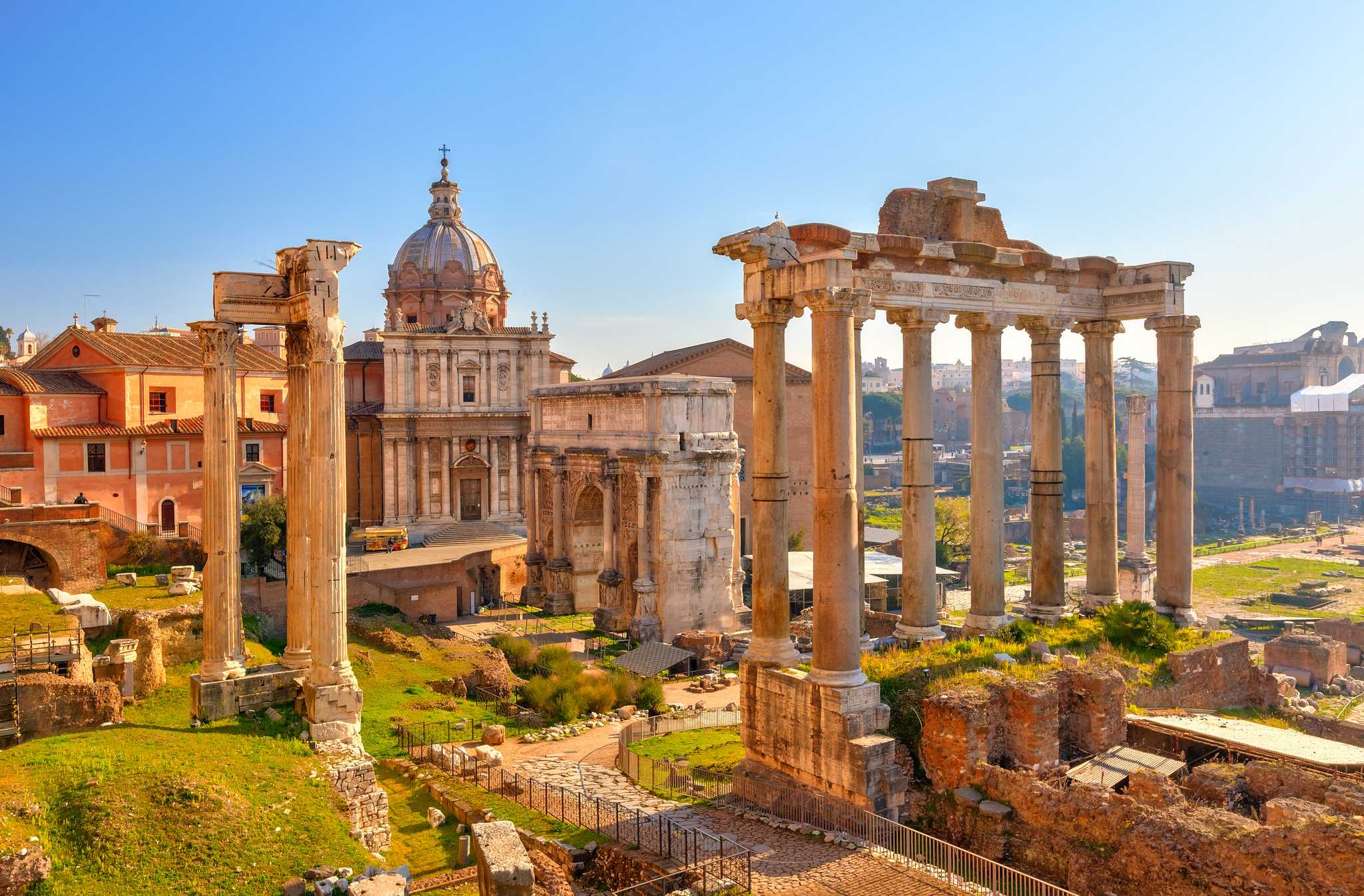 The Roman Forum ruins on a sunny day beneath a blue sky.