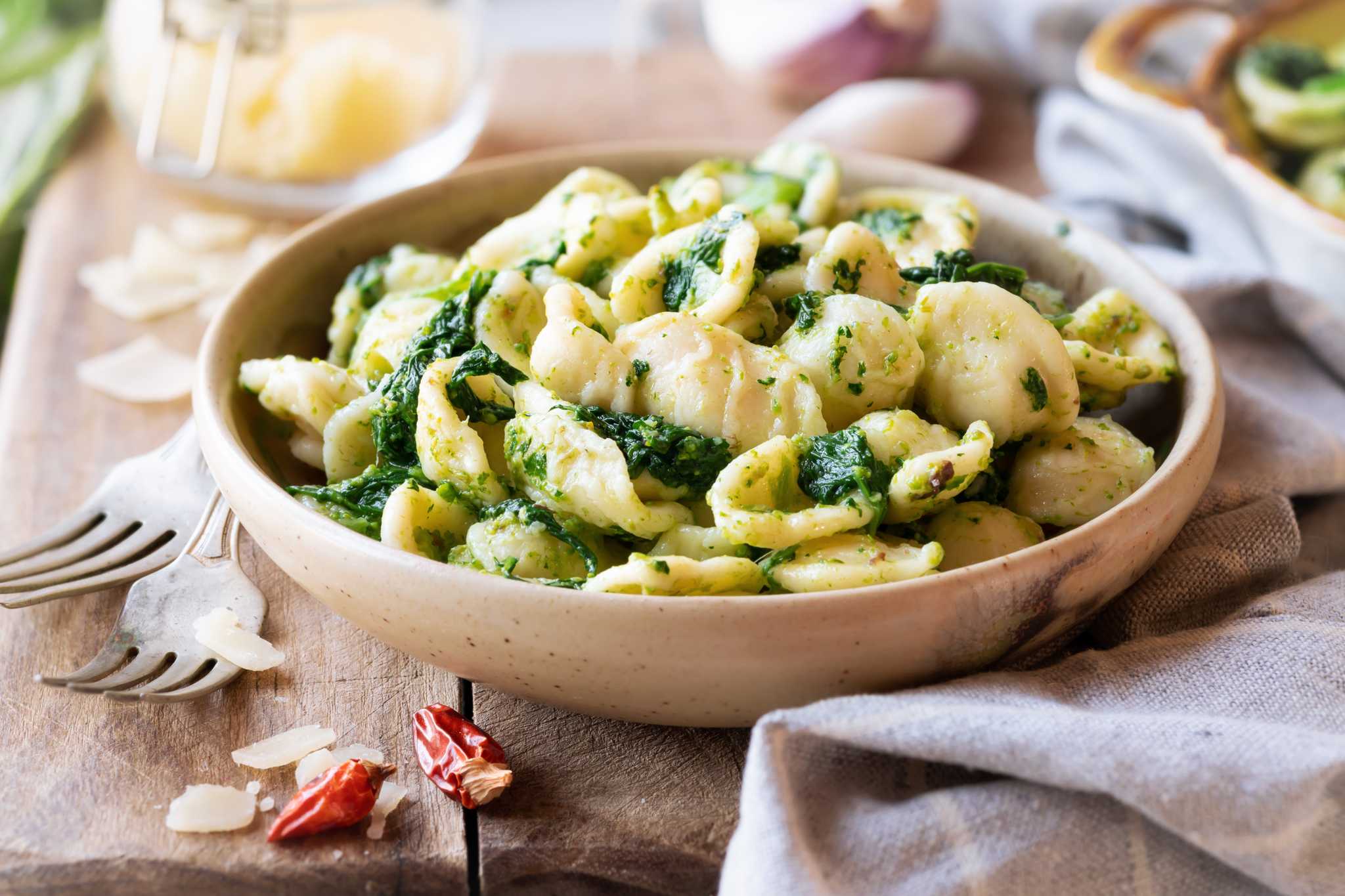 Orecchiette con Cime di Rapa in a bowl beside a cloth and two forks atop a wooden table.