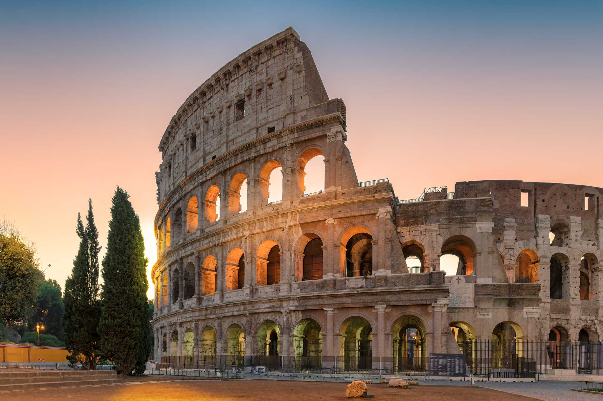 Sunset view of the jagged edge of Rome’s Colosseum with sunlight filtering through the arches.