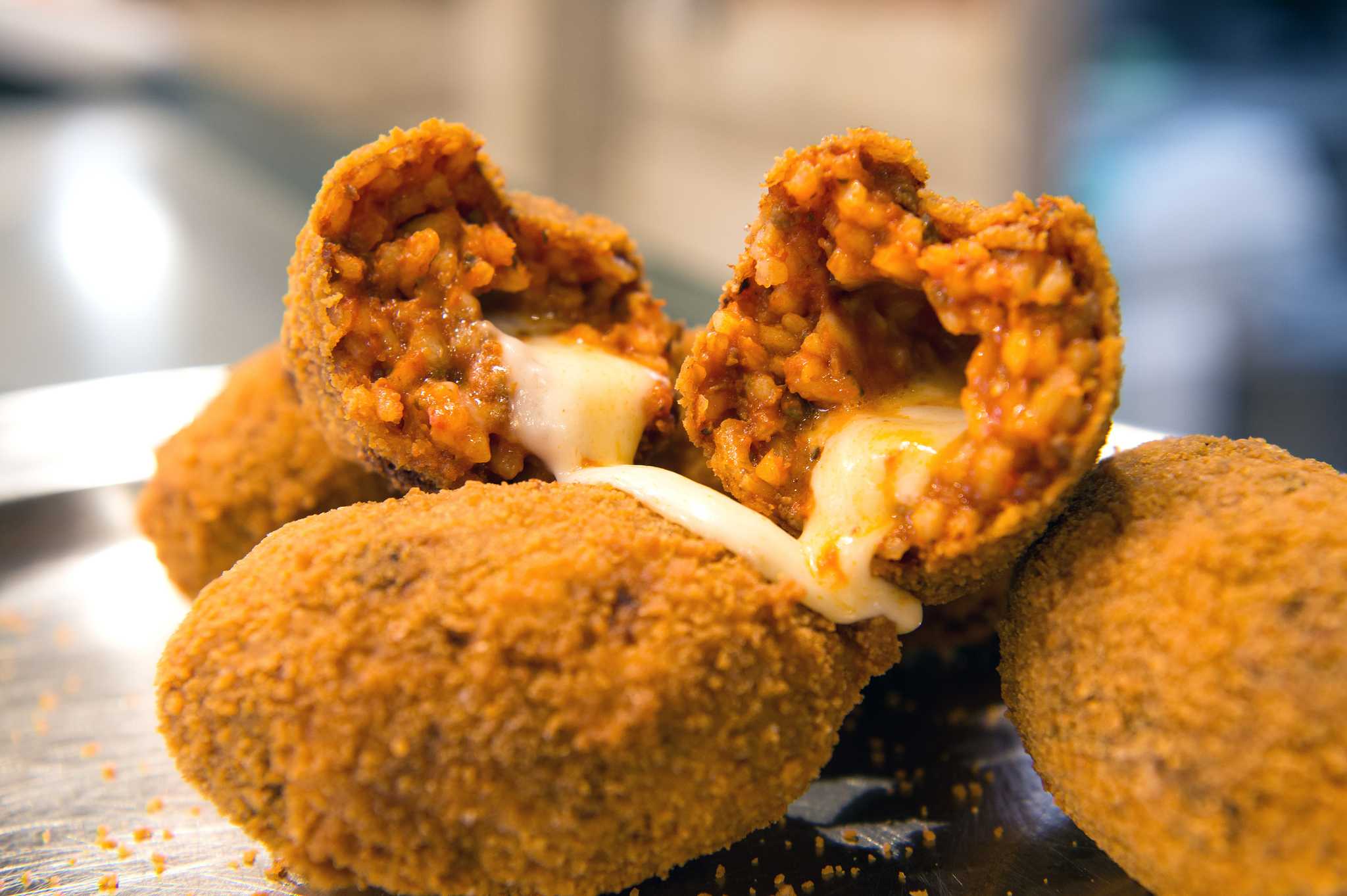 Fried suppli broken open to show the tomato rice and a stretchy molten mozzarella center.