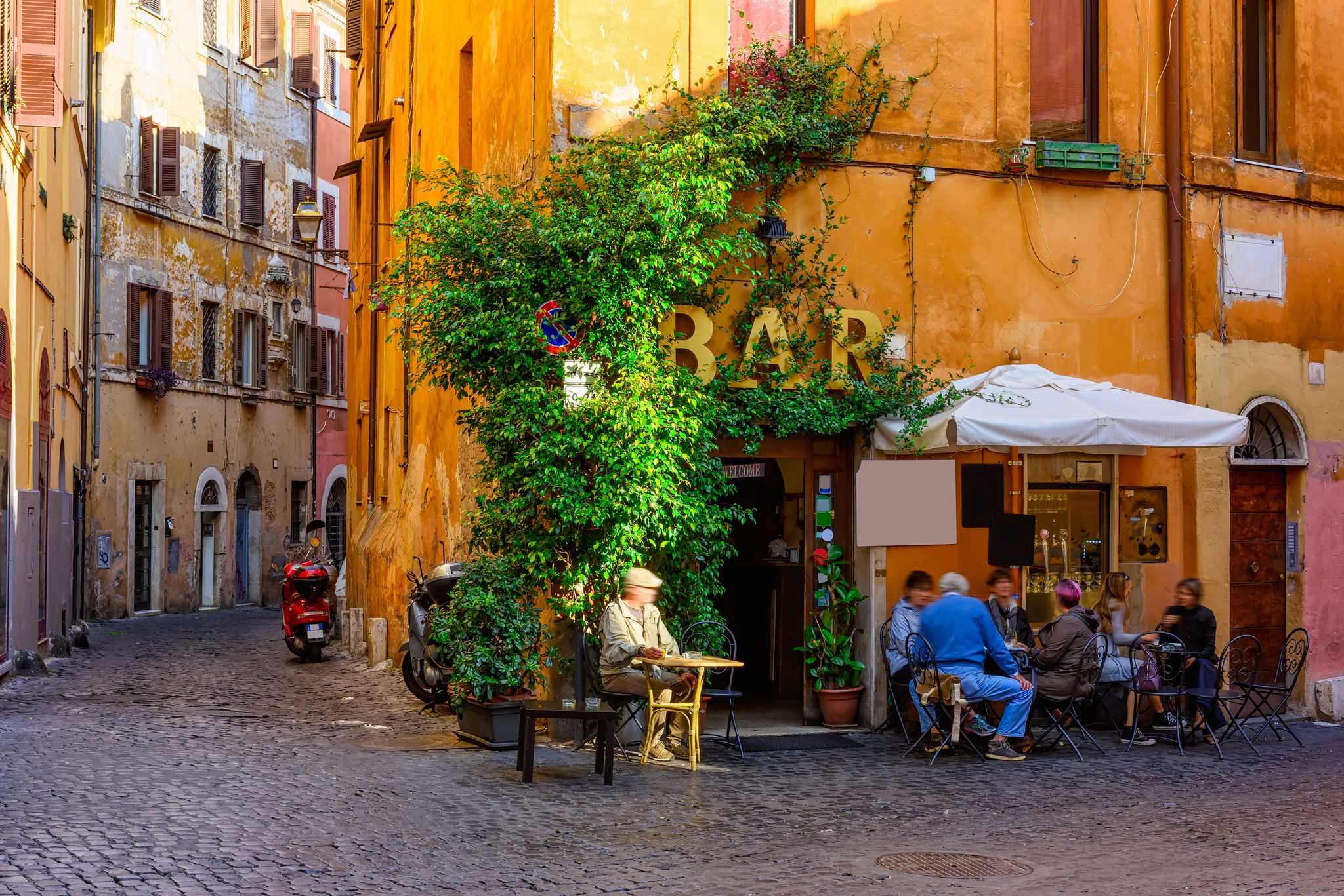 People at an outdoor bar on a cobbled Trastevere corner, ivy climbing an ochre facade.