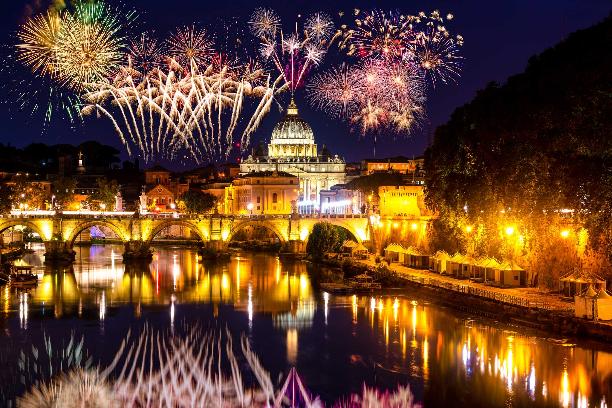 Fireworks show above Sant'Angelo Bridge and St. Peter's Cathedral in Vatican City, reflected in the river below.