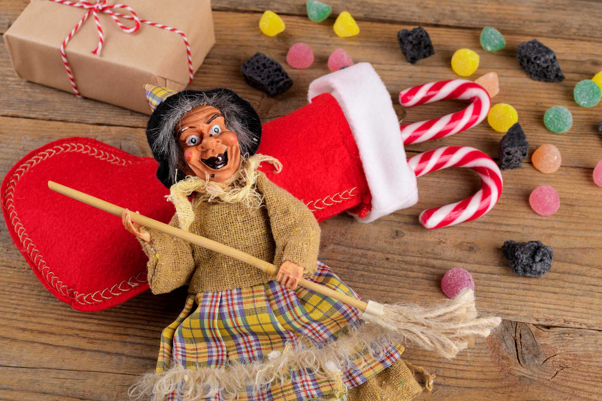 La Befana figurine on top of a stocking, with candies and coal pieces scattered around.