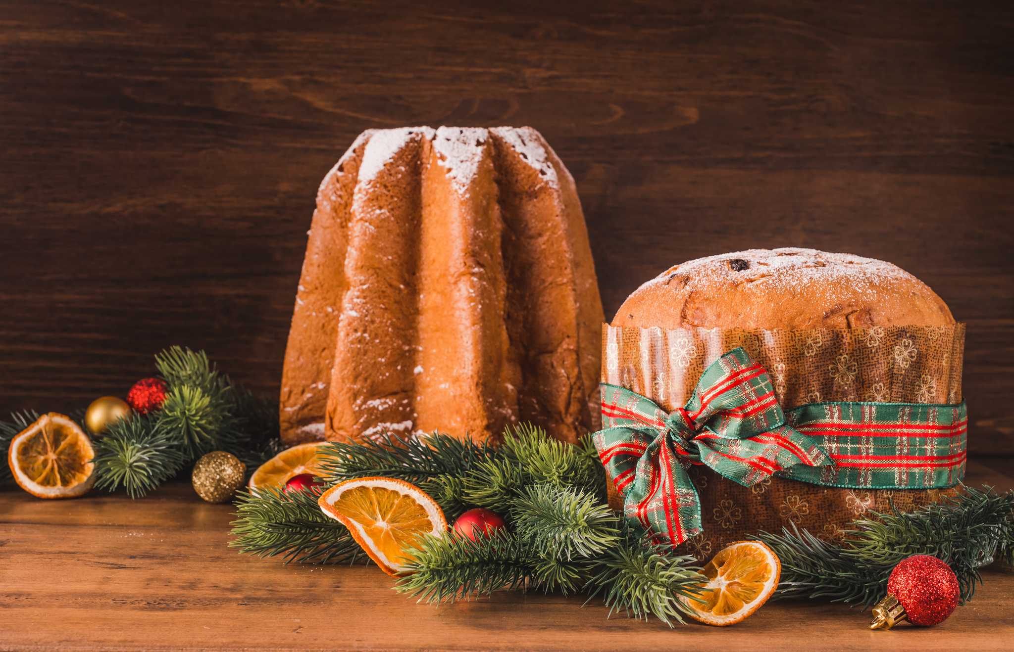 Panettone and pandoro side by side on a table, with festive decorations around.