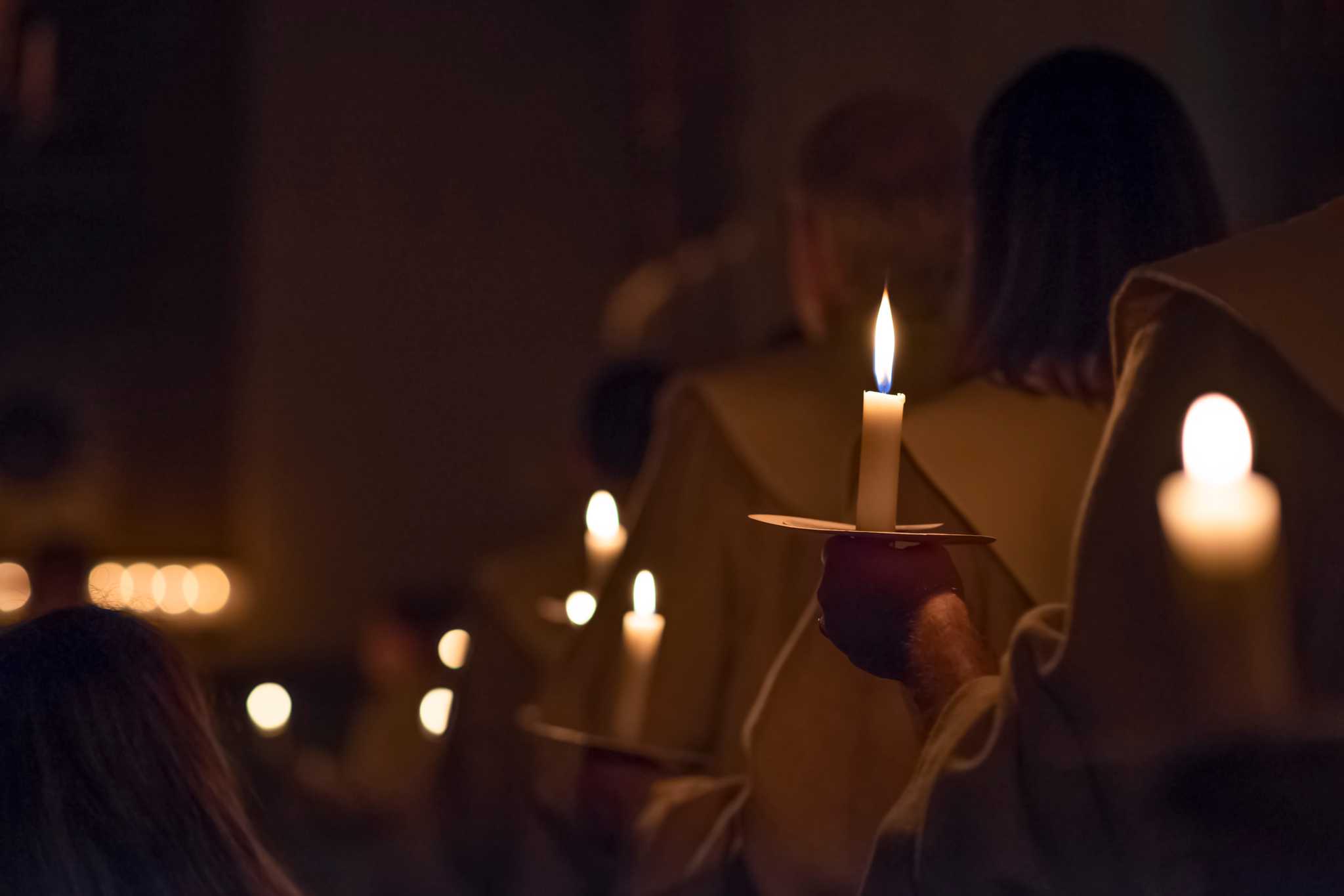 People holding candles in a dimly lit church during the Feast of Santa Lucia.