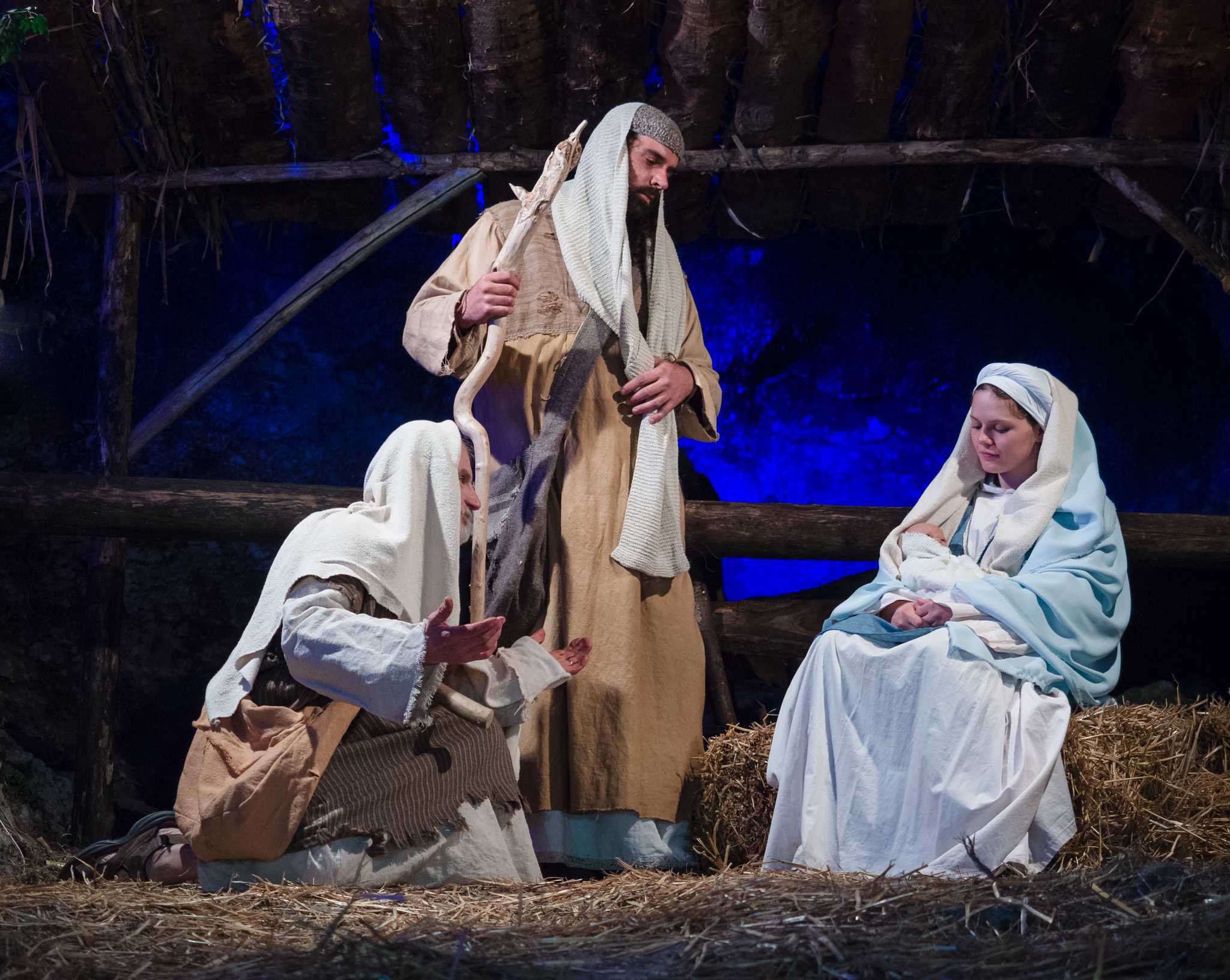 Live nativity scene with three actors in costume standing in a manger.