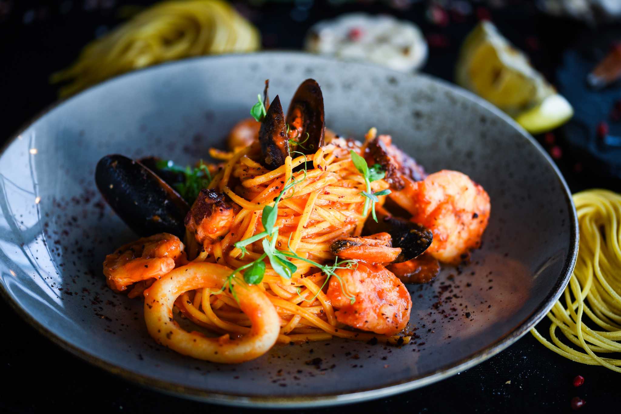 Close-up of a seafood pasta with shrimp and mussels in a blue bowl.