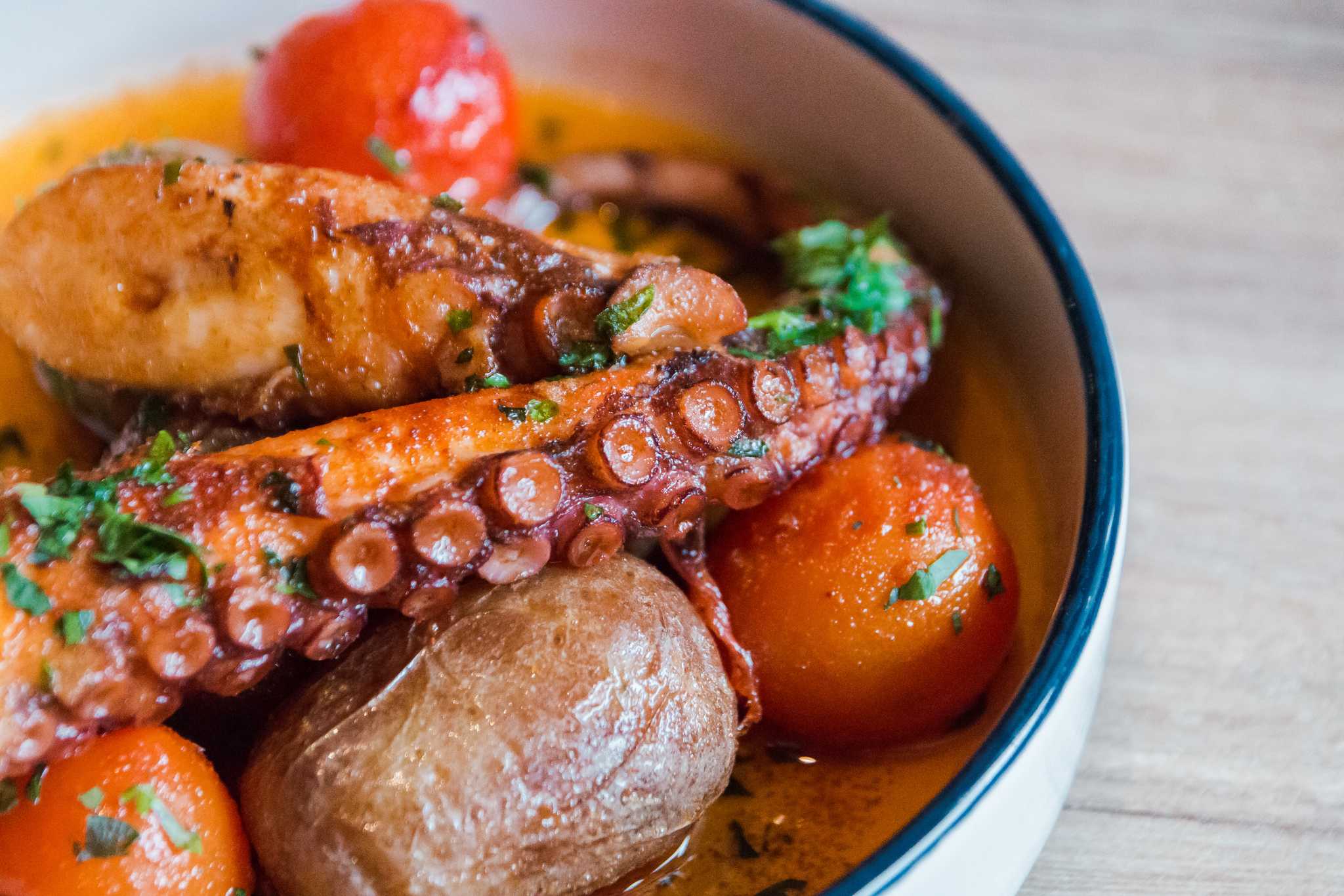 Baked octopus tentacles with tomatoes and potatoes in a white dish.