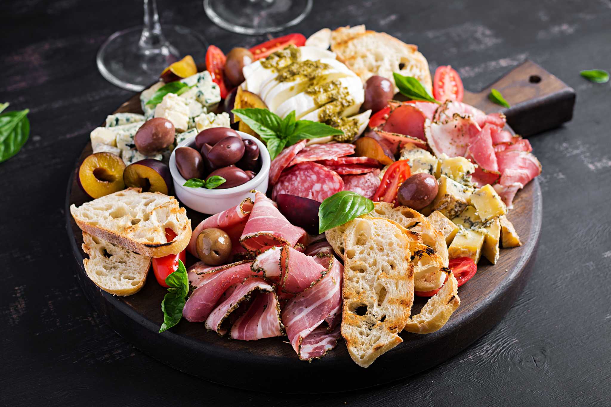 Round wooden board with meat and cheese charcuterie, garnished with basil leaves.