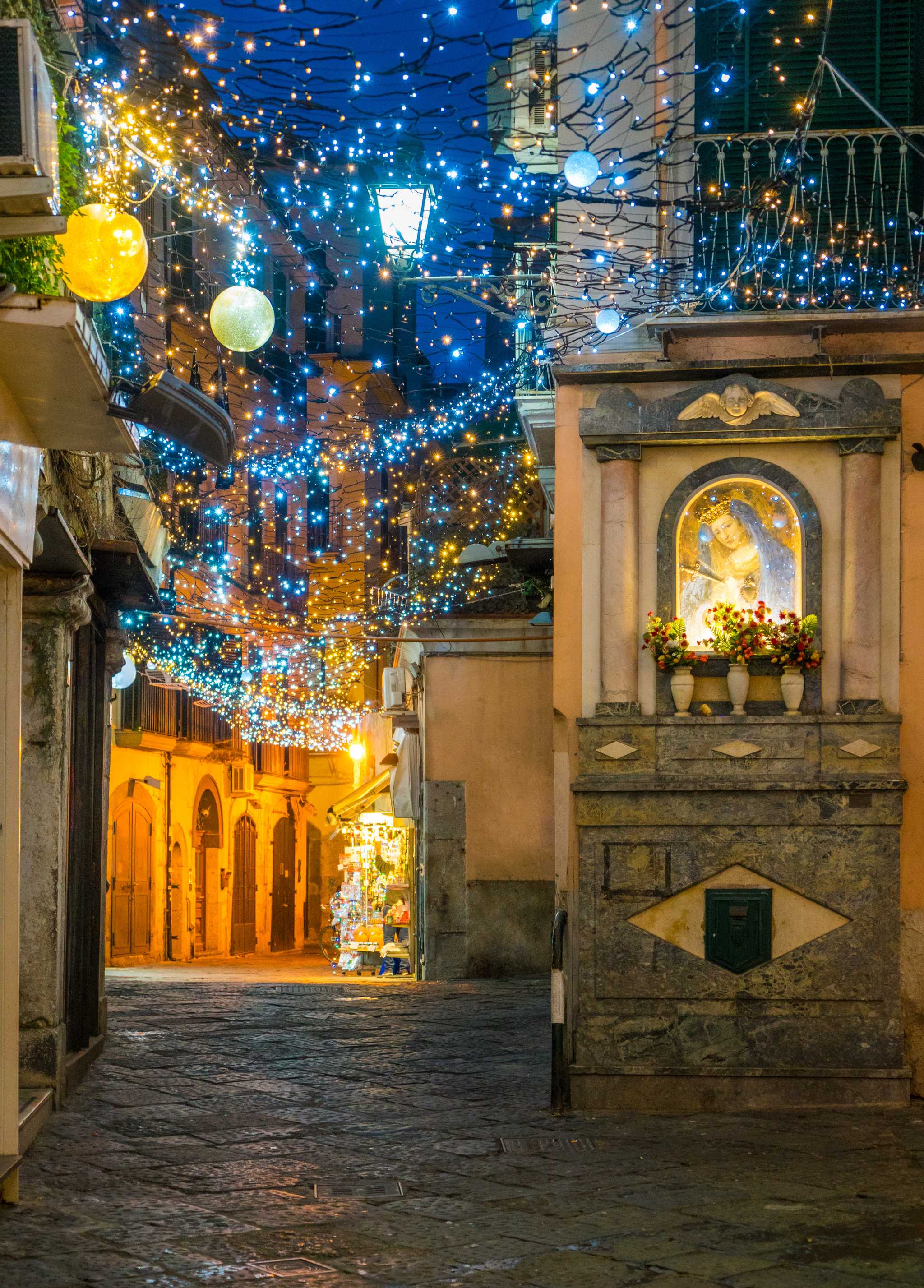 Warm and cool white lights hanging over a cobblestone alley in Salerno, Italy.