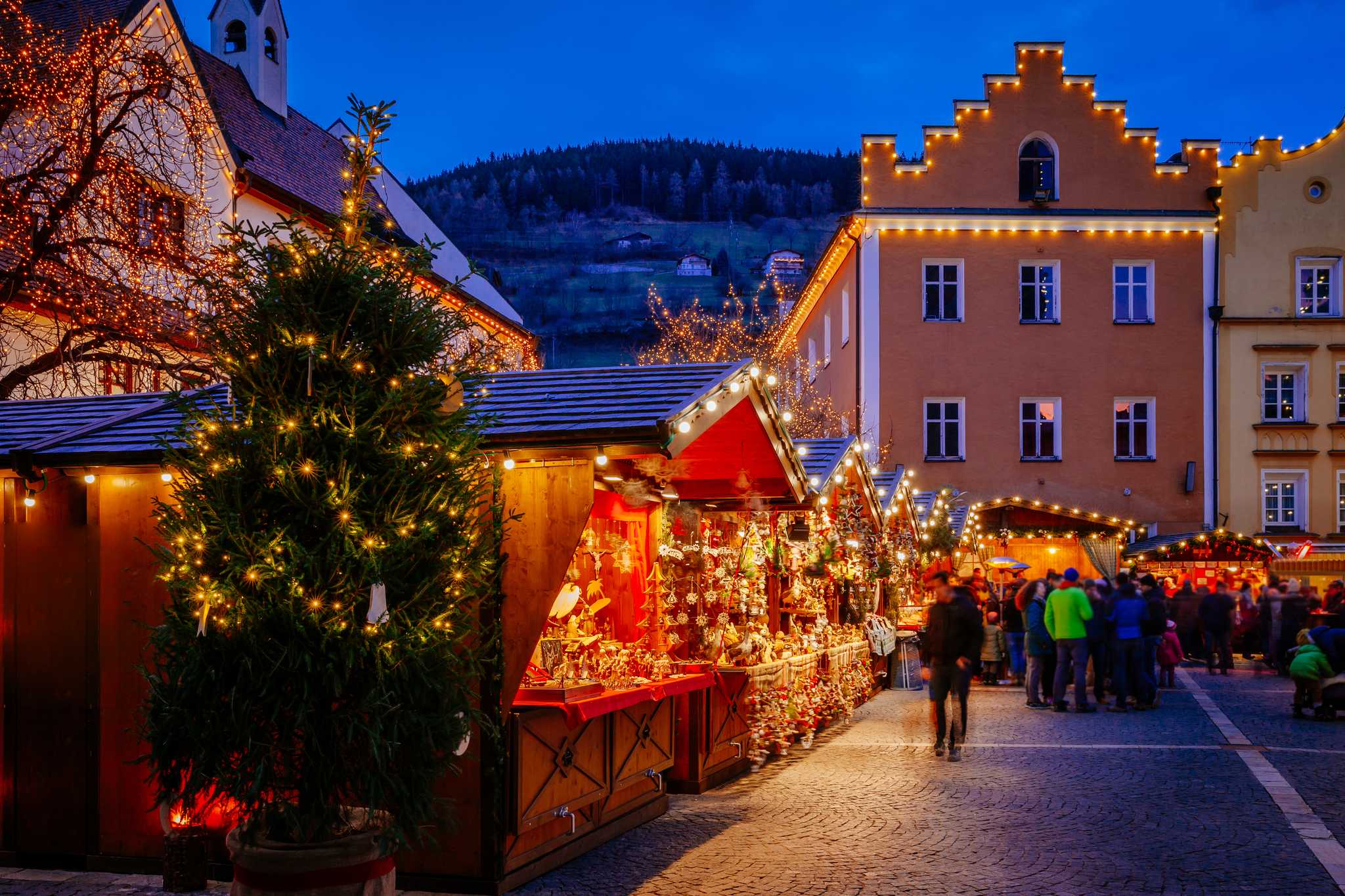 Christmas market in Bolzano with warm lights on a Christmas tree and distant snowy peaks.