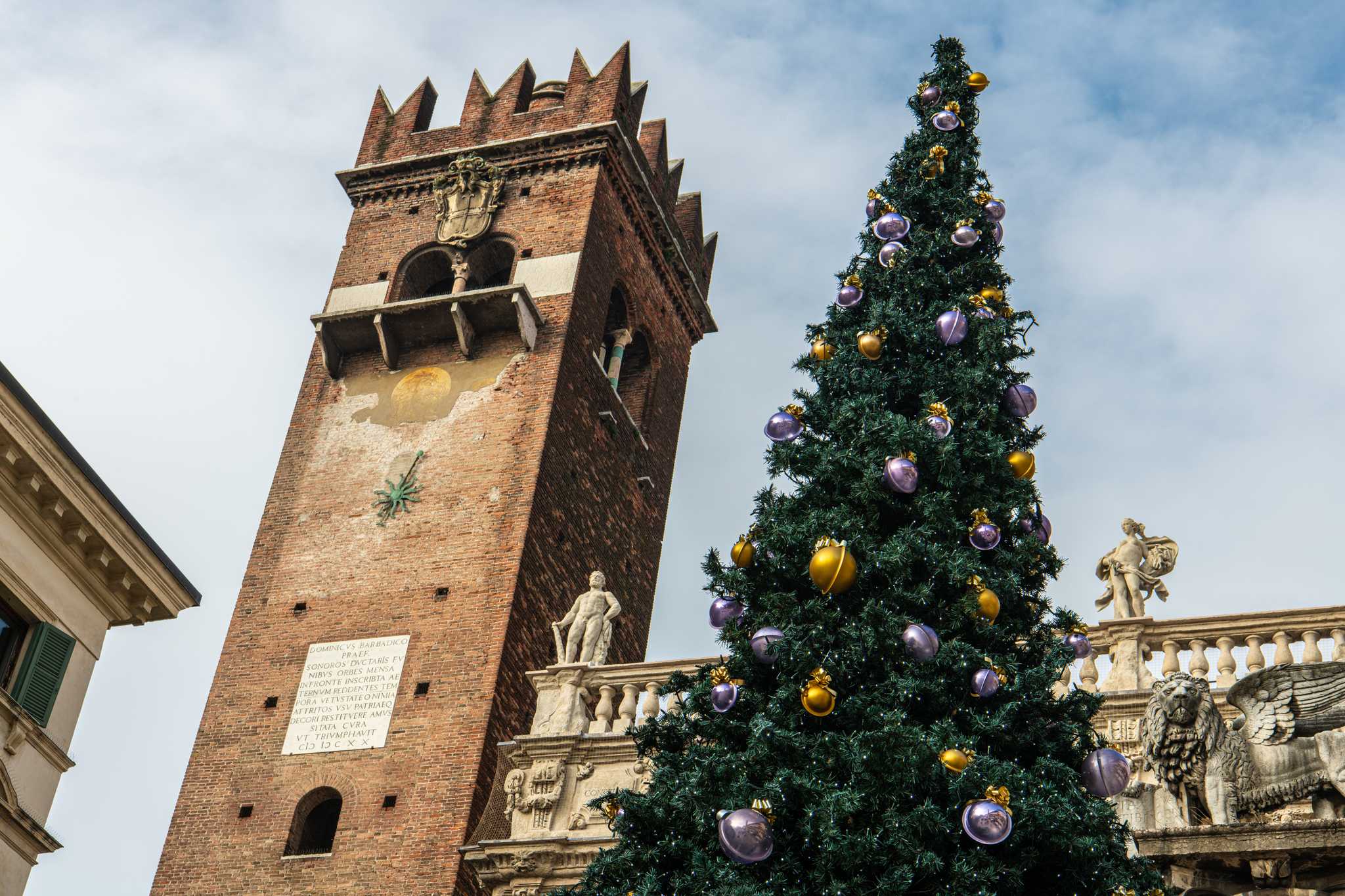 Angled shot of a decorated Christmas tree beside a central tower in Verona.