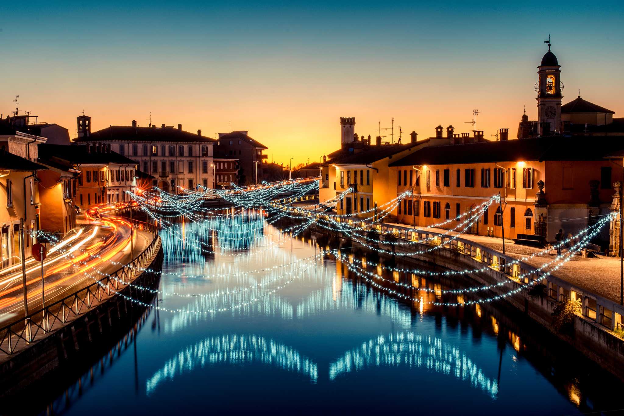 Cool white Christmas lights draped over Navigli canals in Milan at dusk.