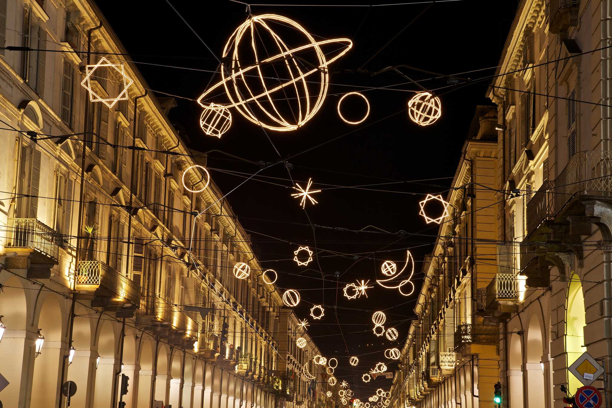Warm white artistic Christmas lights in various shapes over a street in Turin.