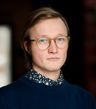 Photo of a person with short light blond-brown hair and round translucent glasses.