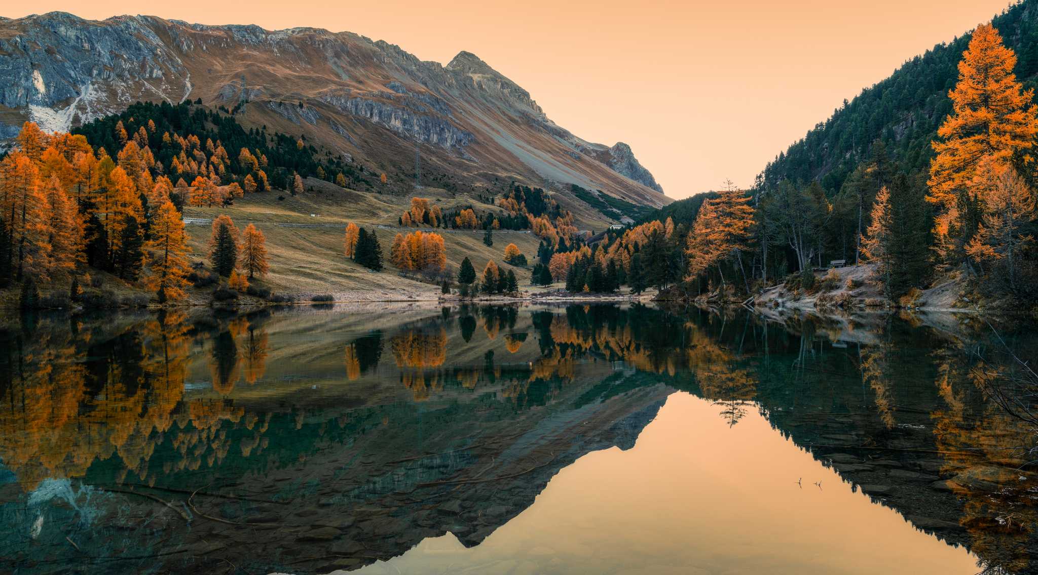 A small lake surrounded by mountains during autumn, with colorful trees all around.