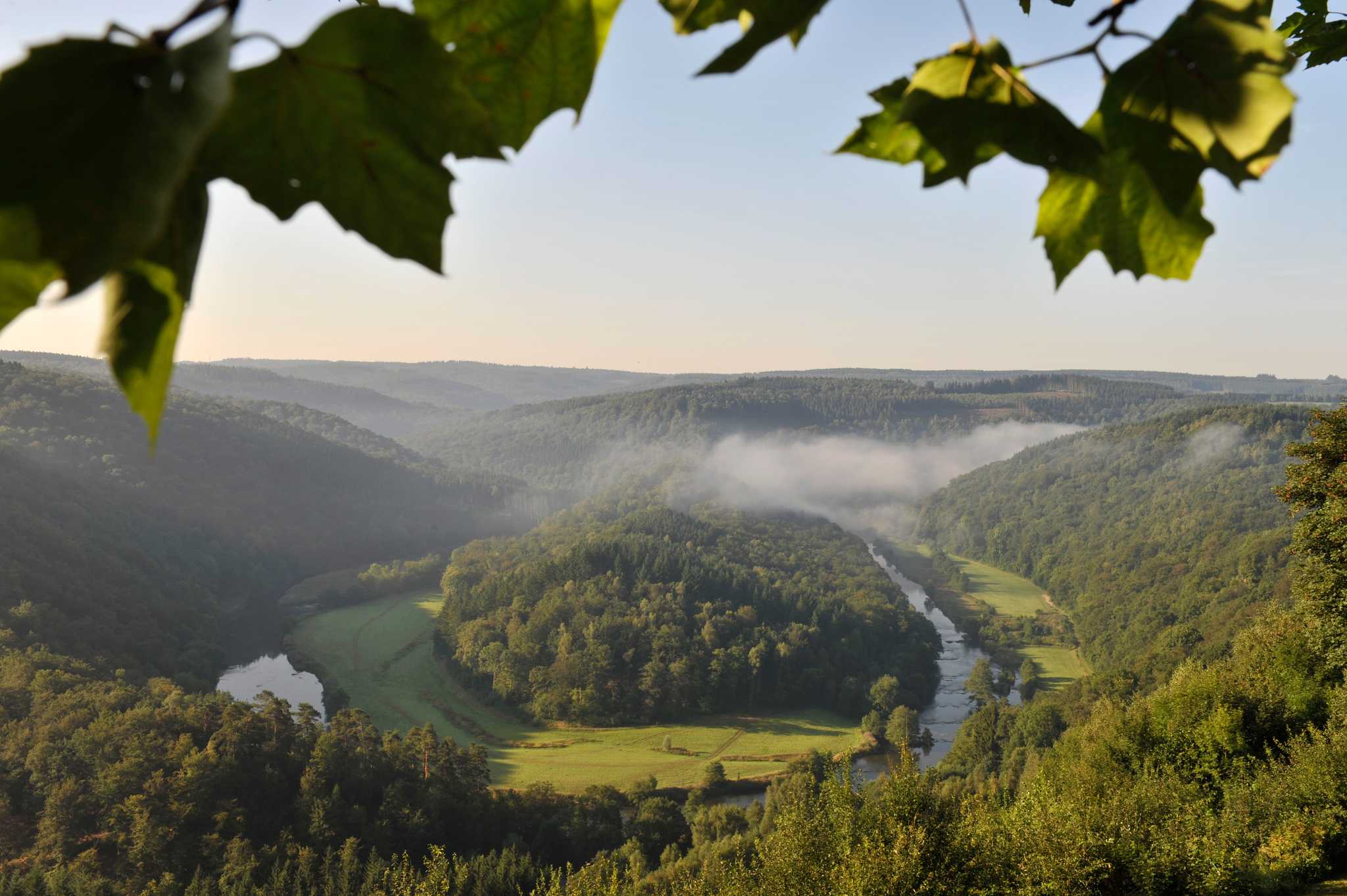 An aerial view of the Semois River meandering through thick forests and hills.