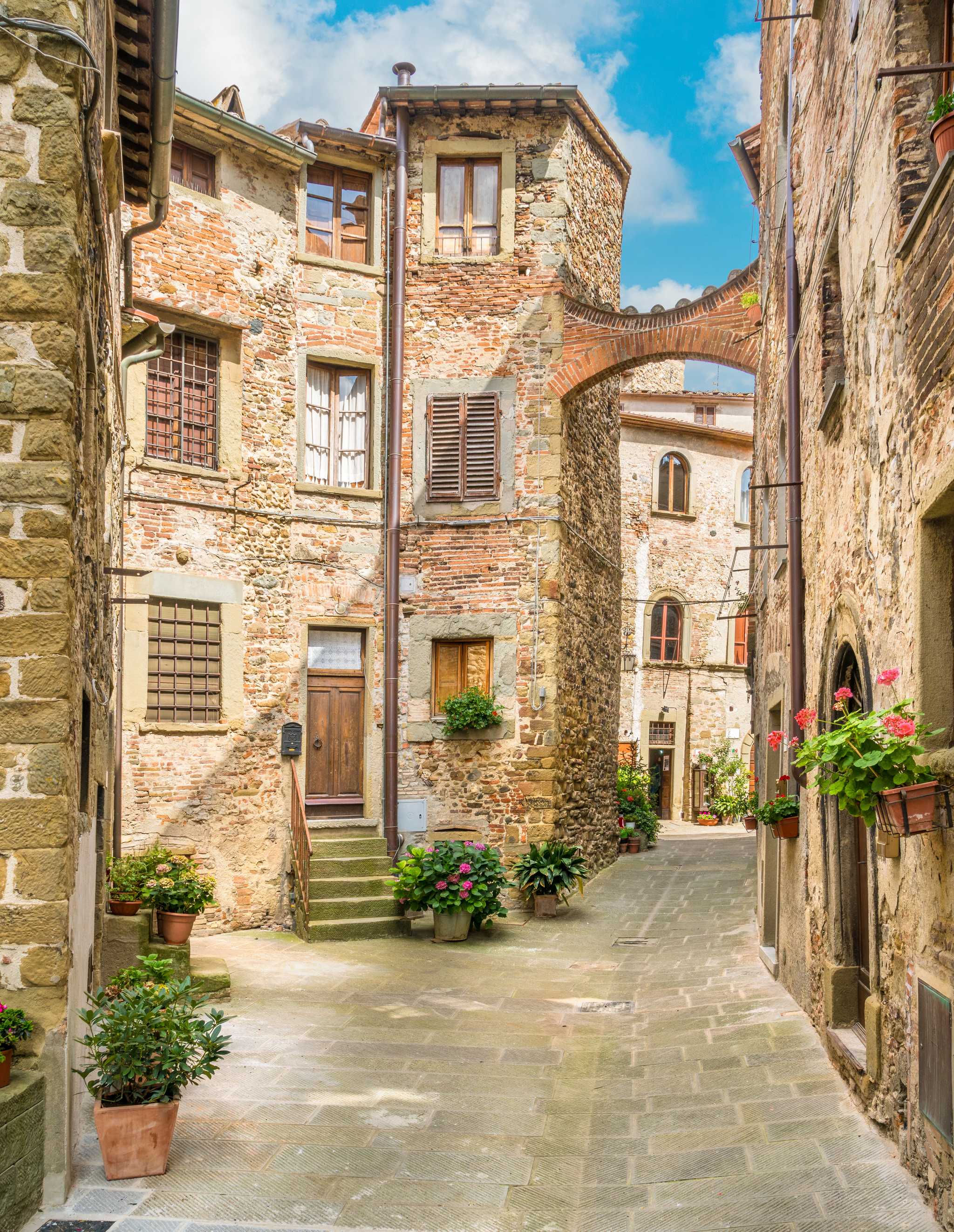 Arezzo alleyway with stone streets and buildings, lined with flowering window boxes.