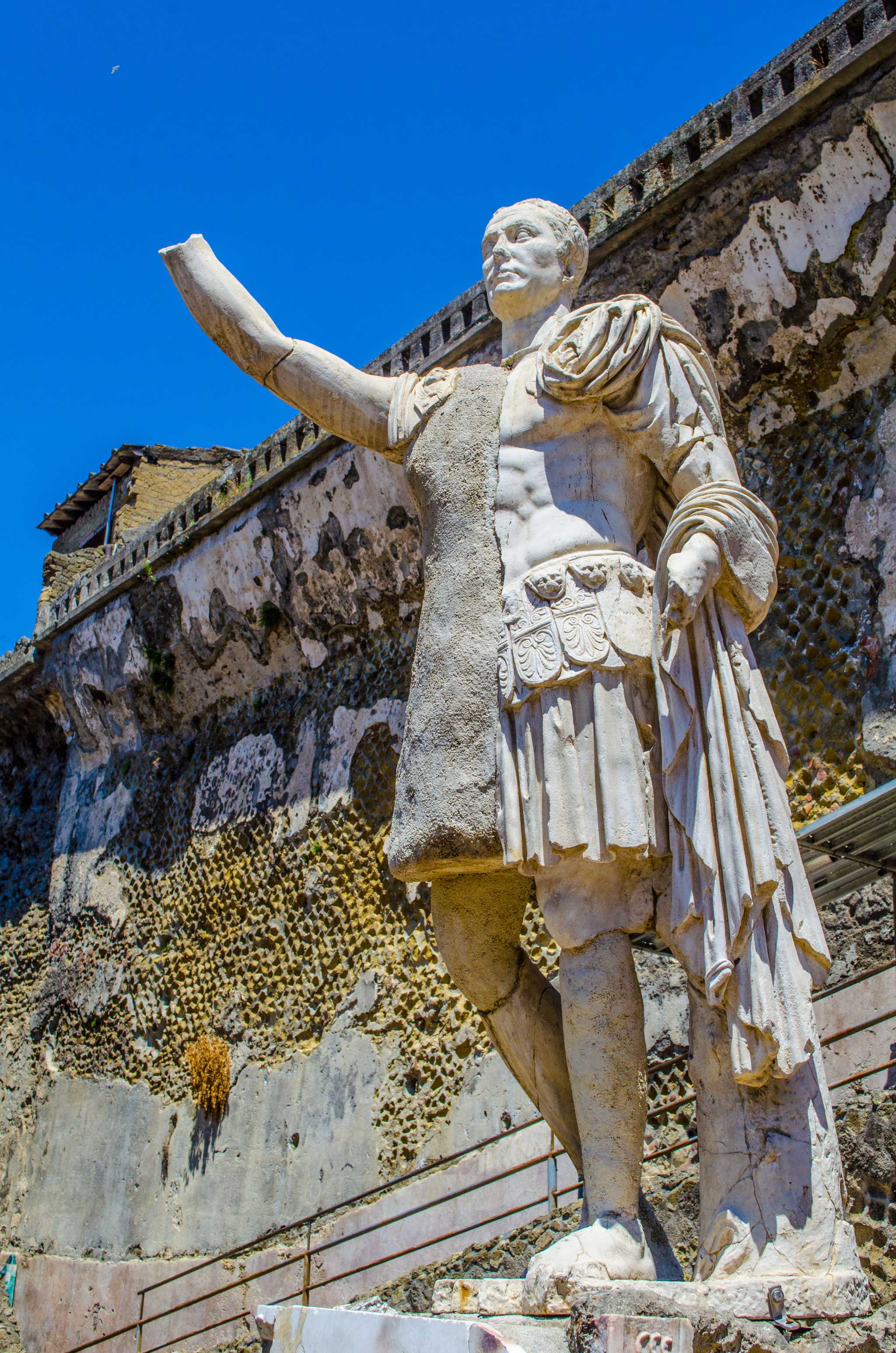 Weathered ancient statue of hero with an arm raised at Herculaneum ruins.