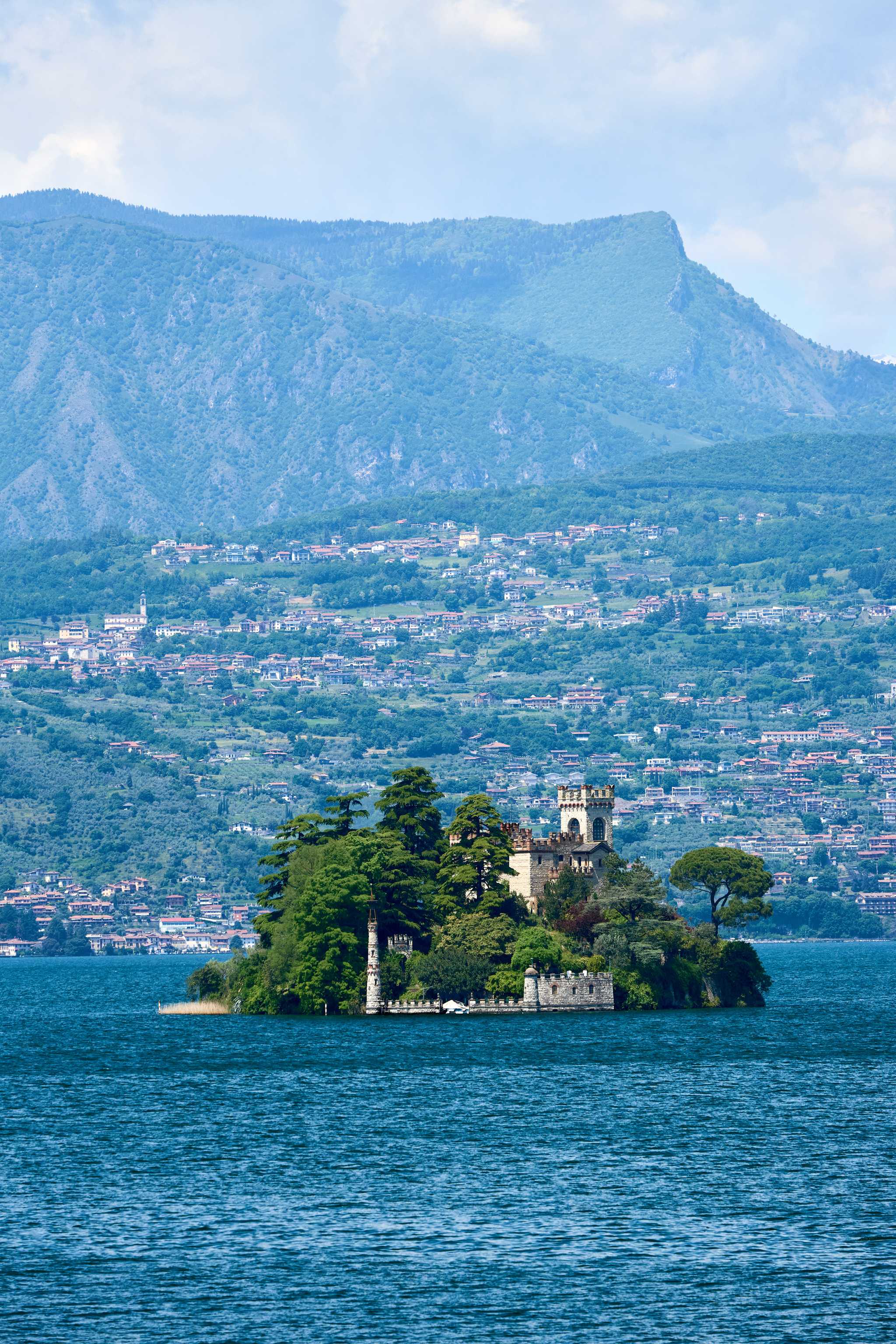 Isola di Loreto, a small island in Lake Iseo with a castle and trees, with hills in the background.