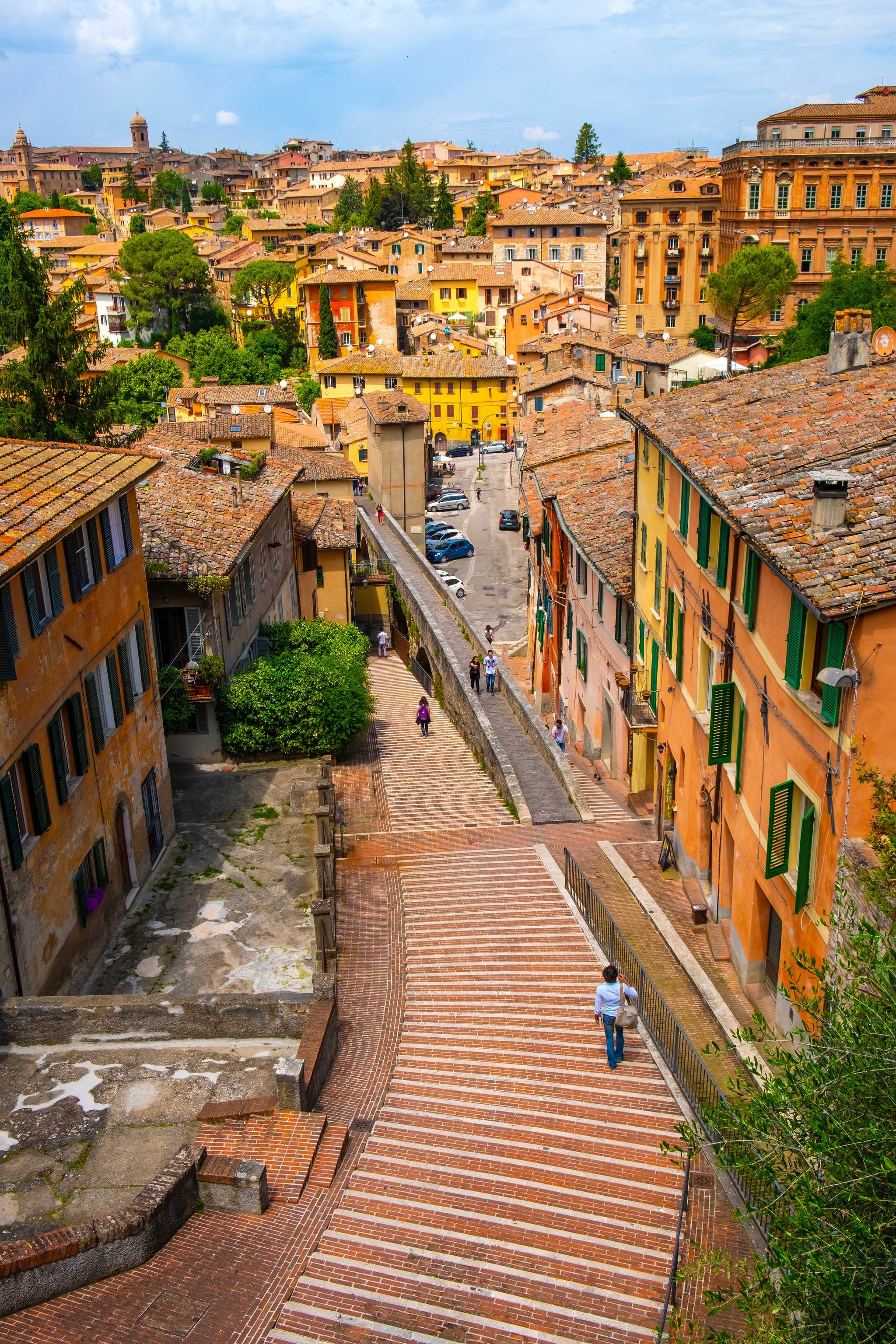 Downward view of descending staircase street in Perugia, lined by orange and yellow buildings.