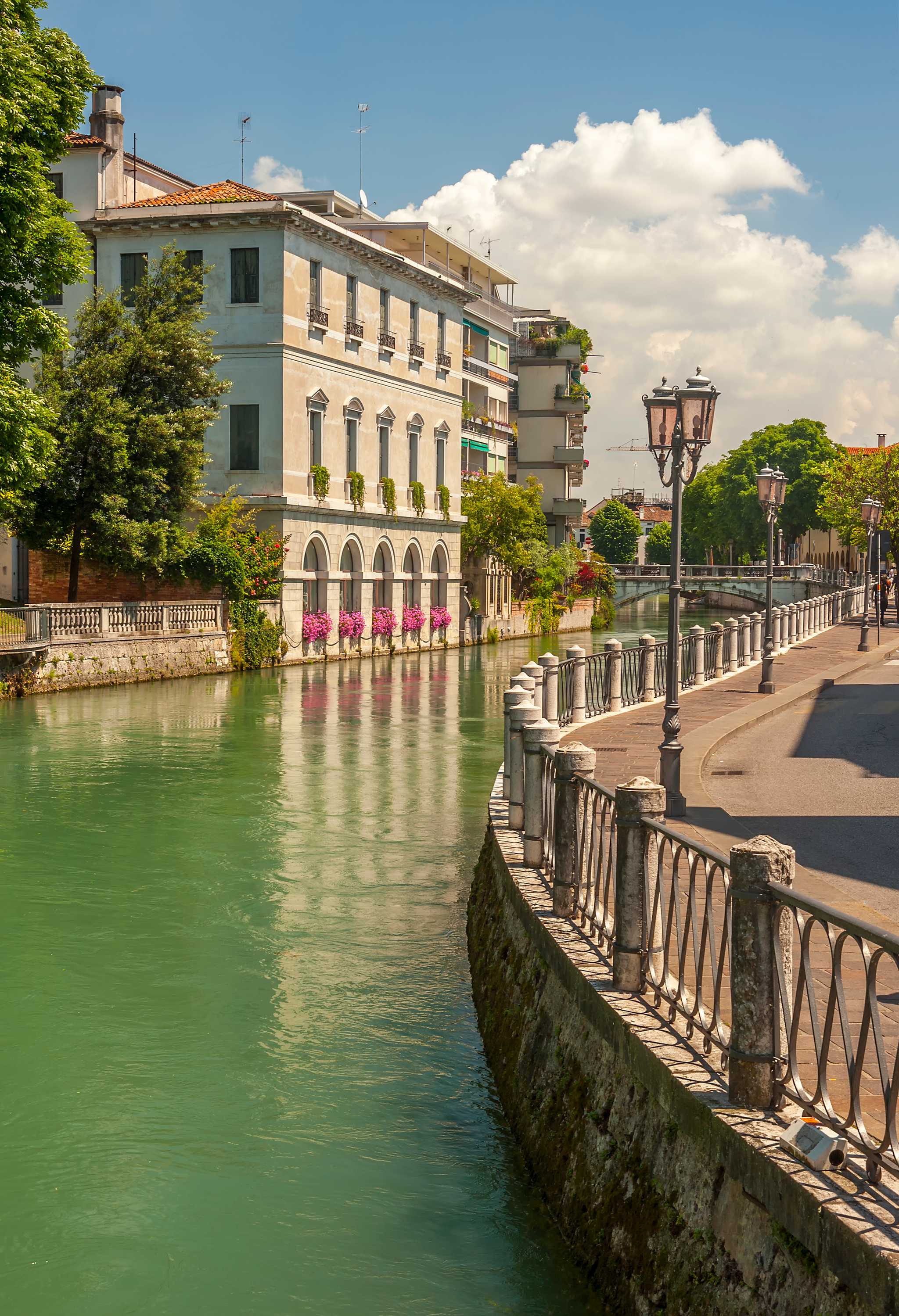 Waterside promenade in Treviso, featuring green water winding along a path with lamposts.