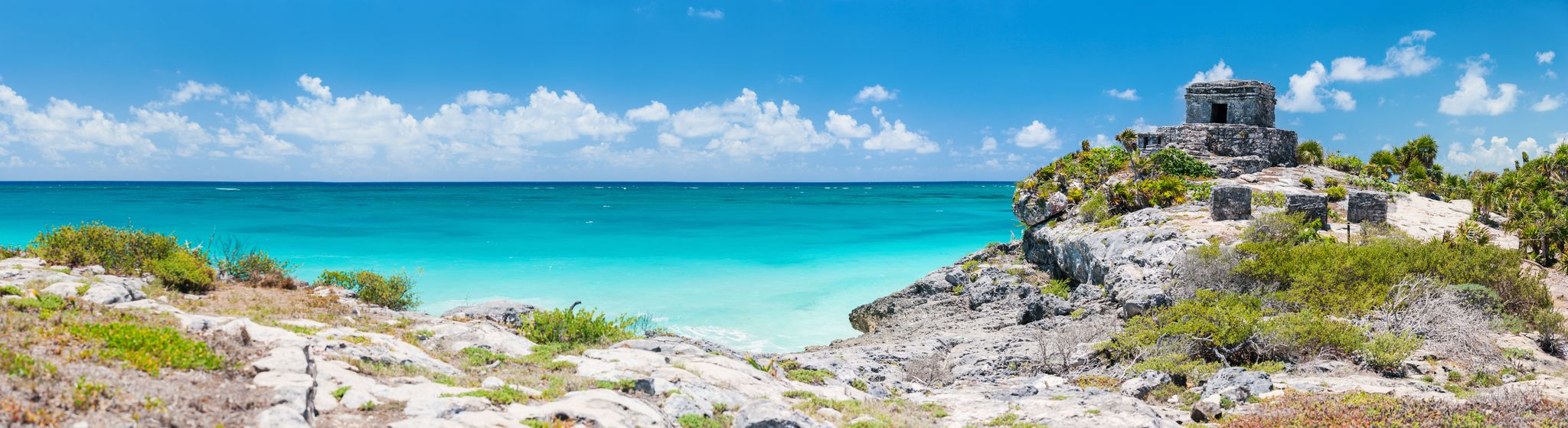 Panorama of Tulum ruins, the sandy beach below, and the blue sea beyond.