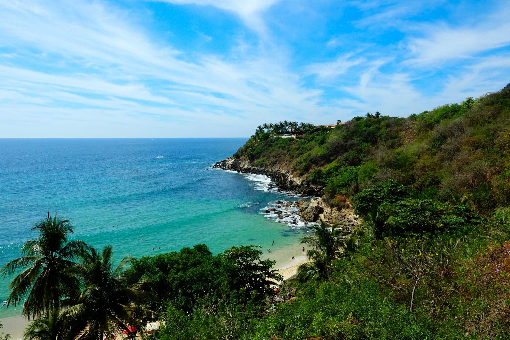 Distant shot of a beach below lush green cliffs in Puerto Escondido.