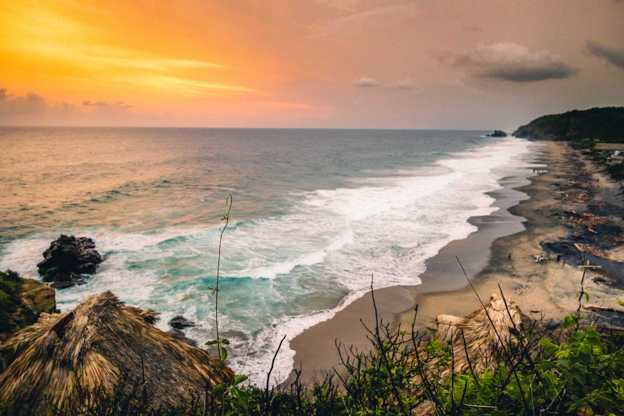 Sunset at a beach in Mazunte, the sky orange and pink above the frothy sea.