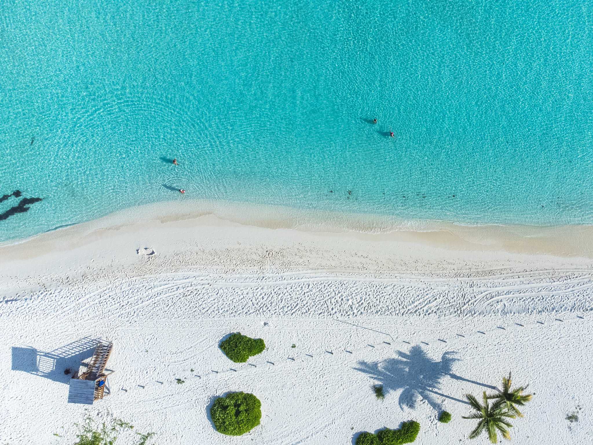Bird's-eye view of a white sand beach in Playa del Carmen, a few swimmers in the water.