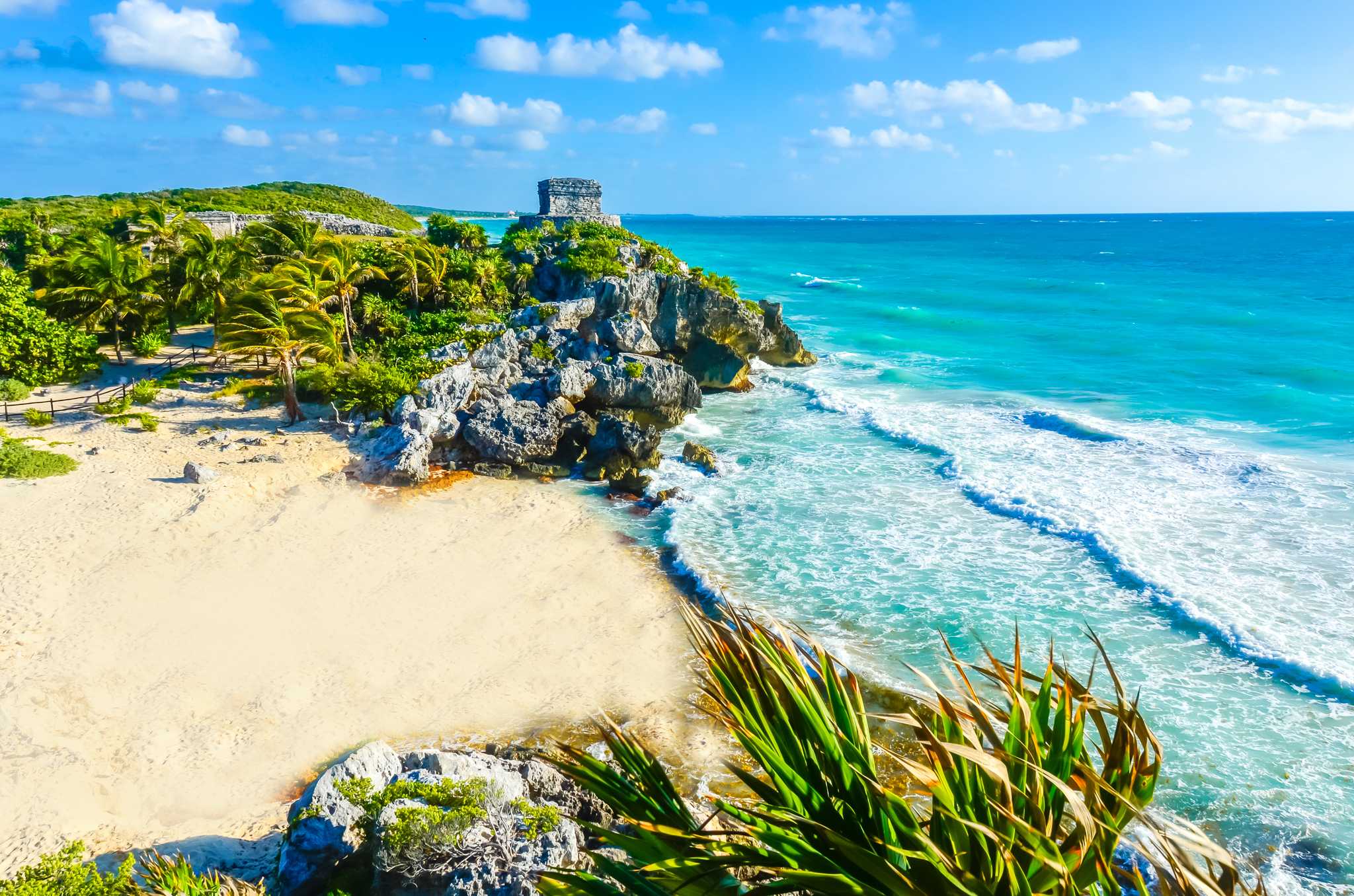 Playa Ruinas in Tulum, white sand and blue water below hilltop ruins.