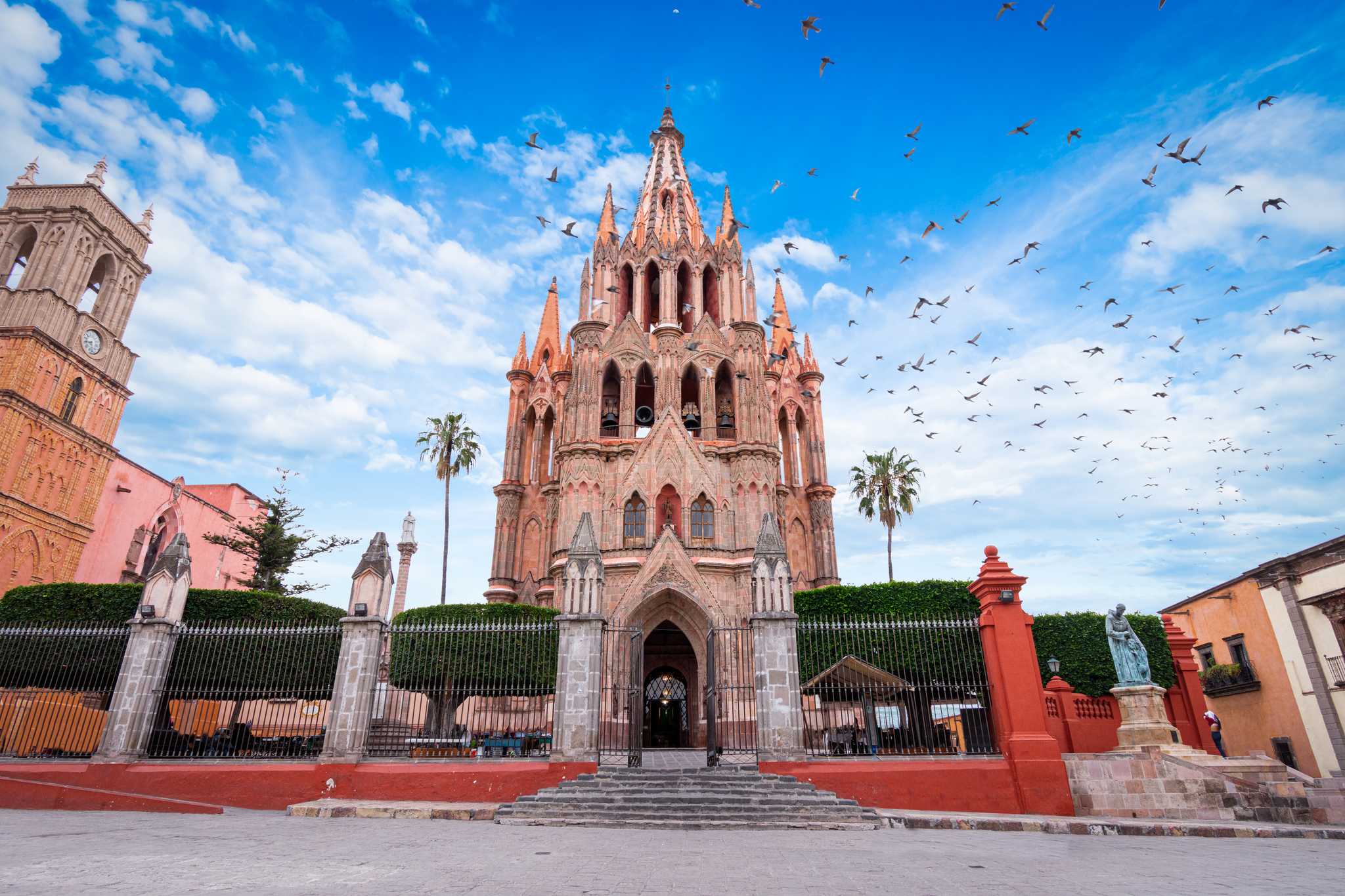 Pink Church of San Miguel de Allende shot from below, flanked by palm trees.