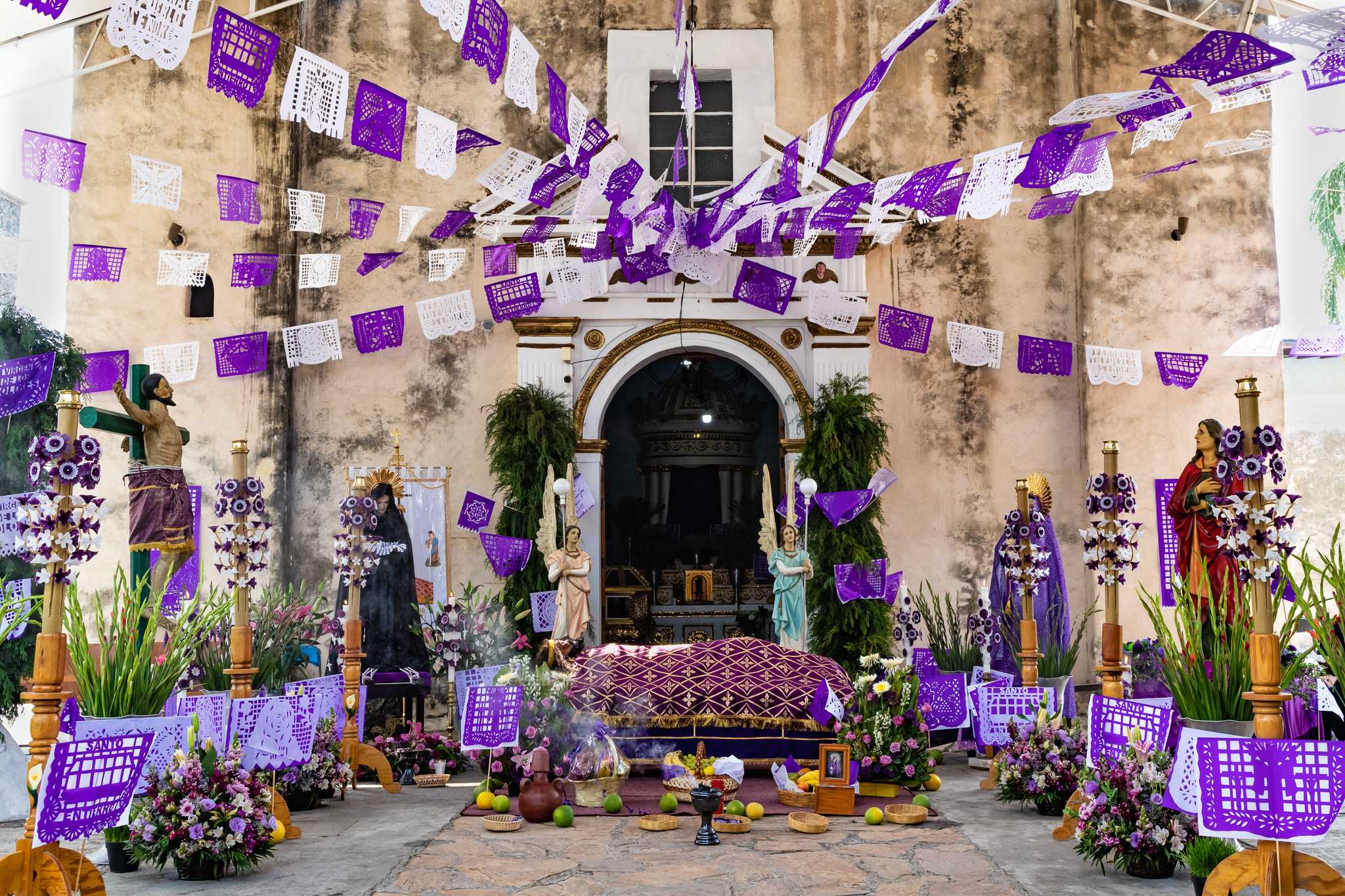 Holy Week altar with purple papel picado, saint statues, and flowers at a Mexican church.
