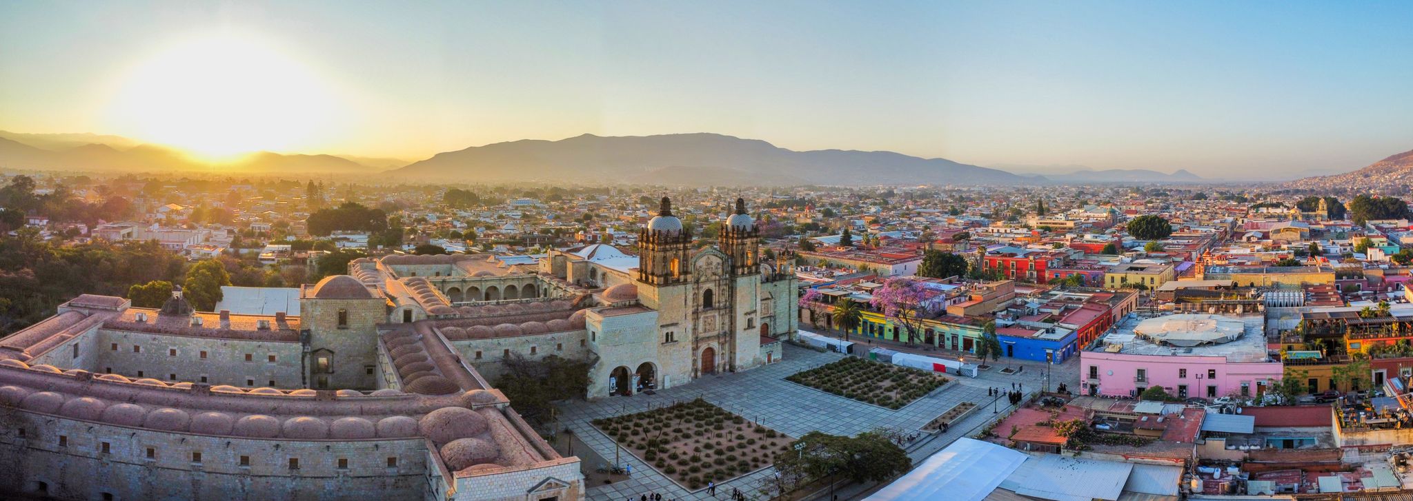 Sun rising above the mountains behind Oaxaca City, lighting the colorful buildings.
