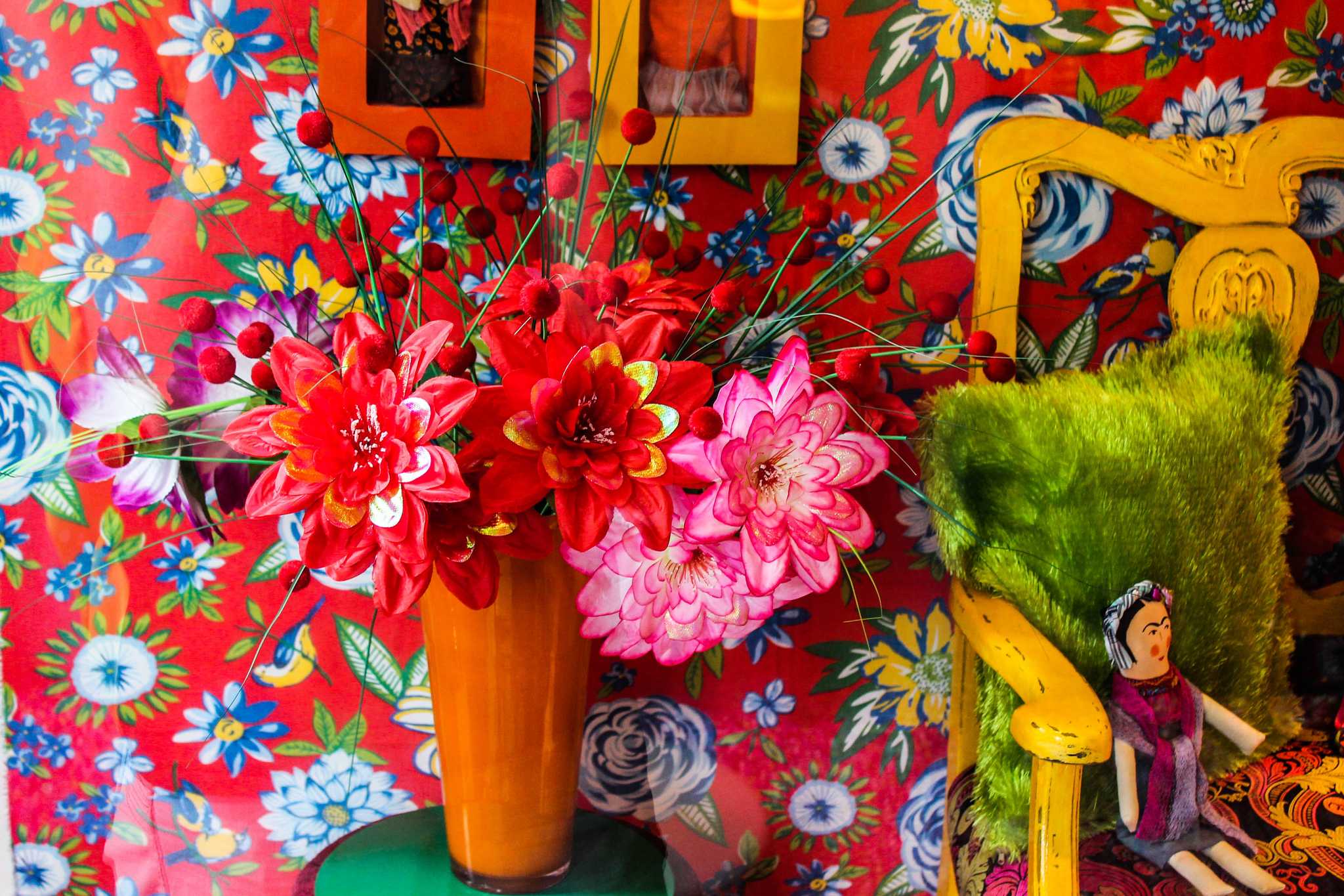 Bright, colorful floral interior of Frida Kahlo house, with busy floral wallpaper and a vase of pink flowers.