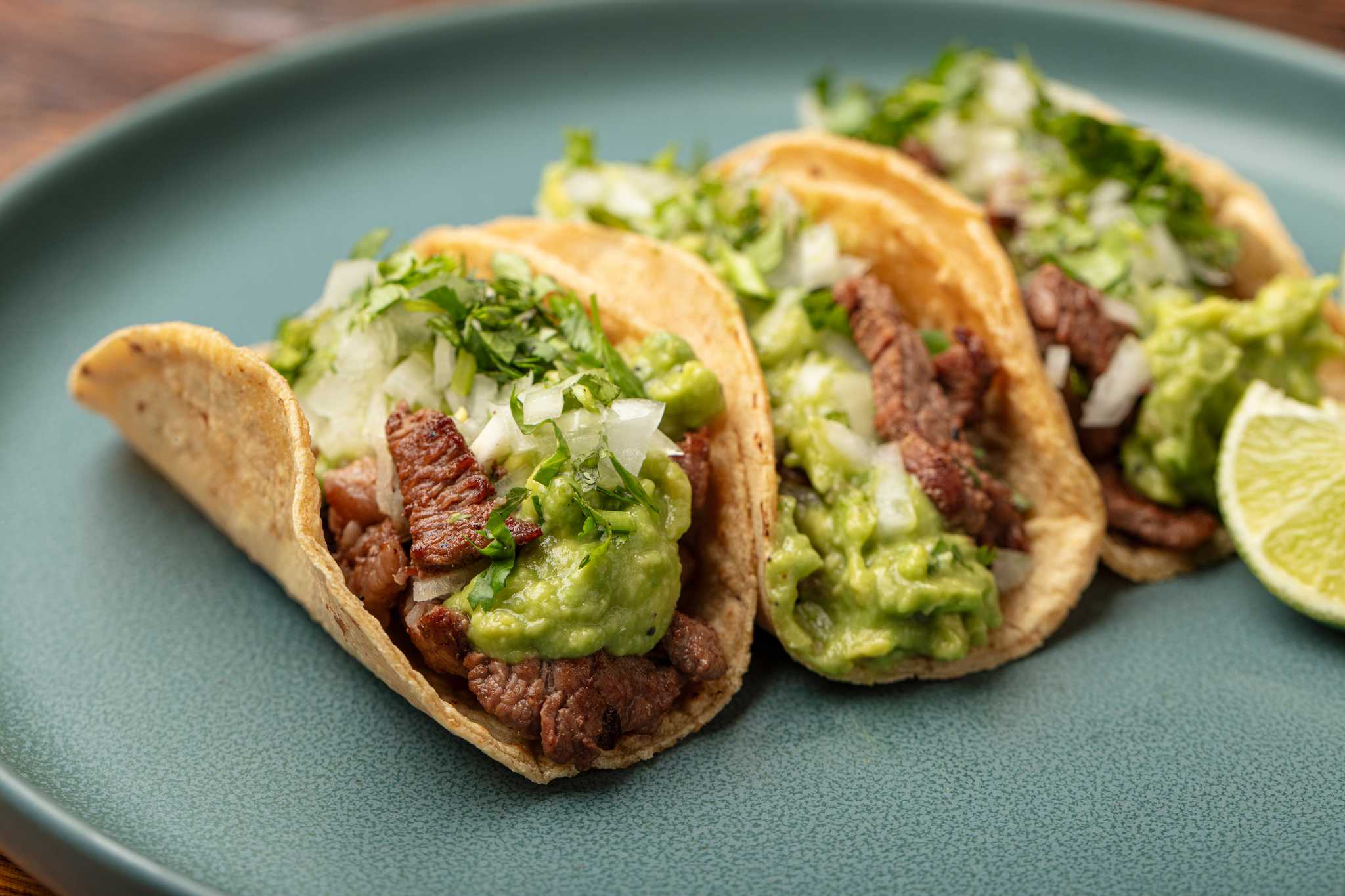 Blue plate with three beef street tacos and a lime wedge.