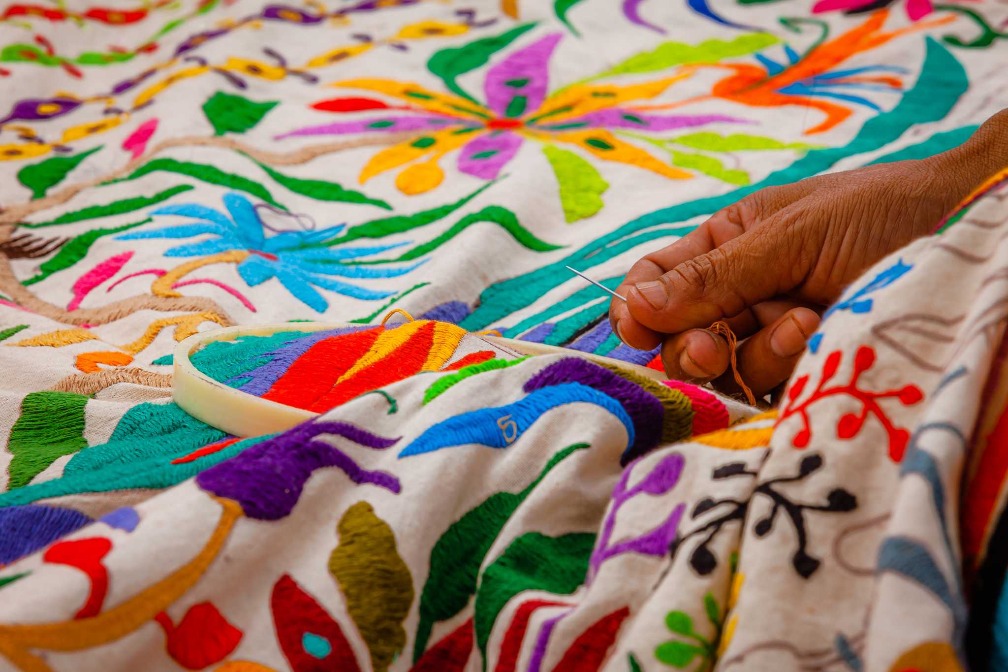 Close-up of a hand embroidering colorful details onto thick white fabric.