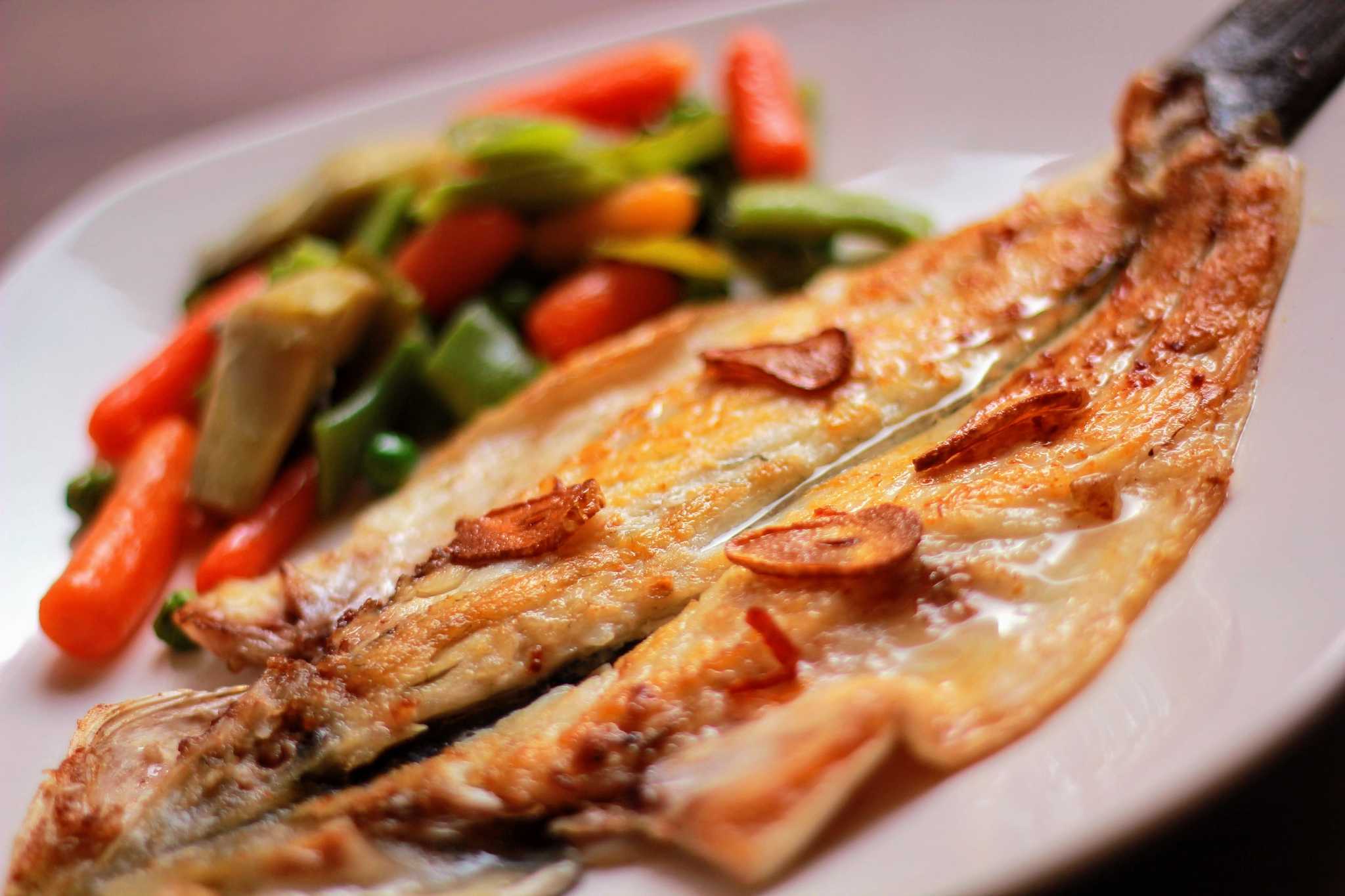 Close-up of grilled butterflied fish fillet with green and red peppers on the side.