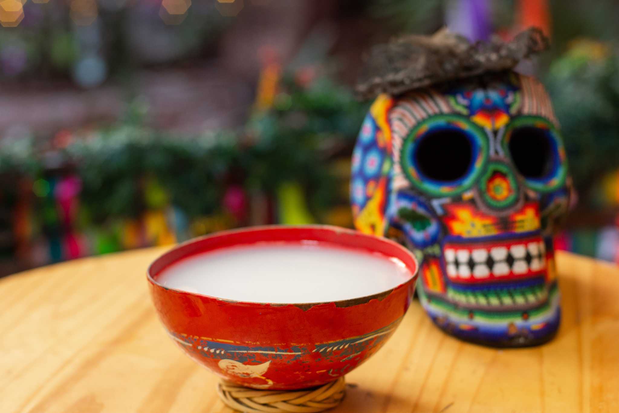 Red cup of pulque on a table beside a colorful Huichol skull.