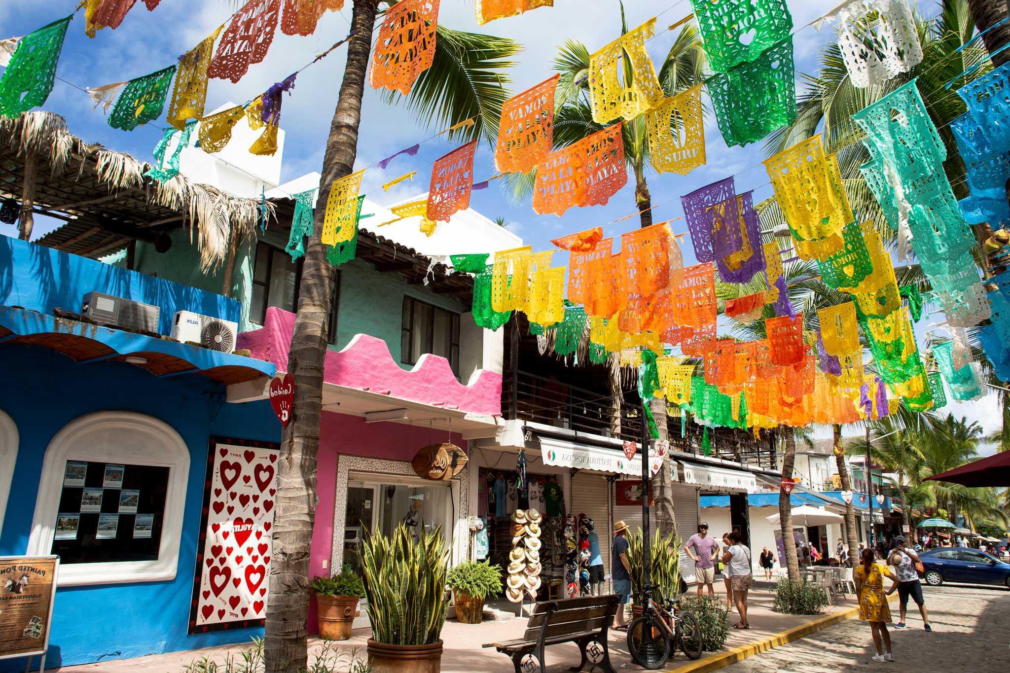 Colorful banners hanging over a street in Sayulita, with blue and pink buildings behind.