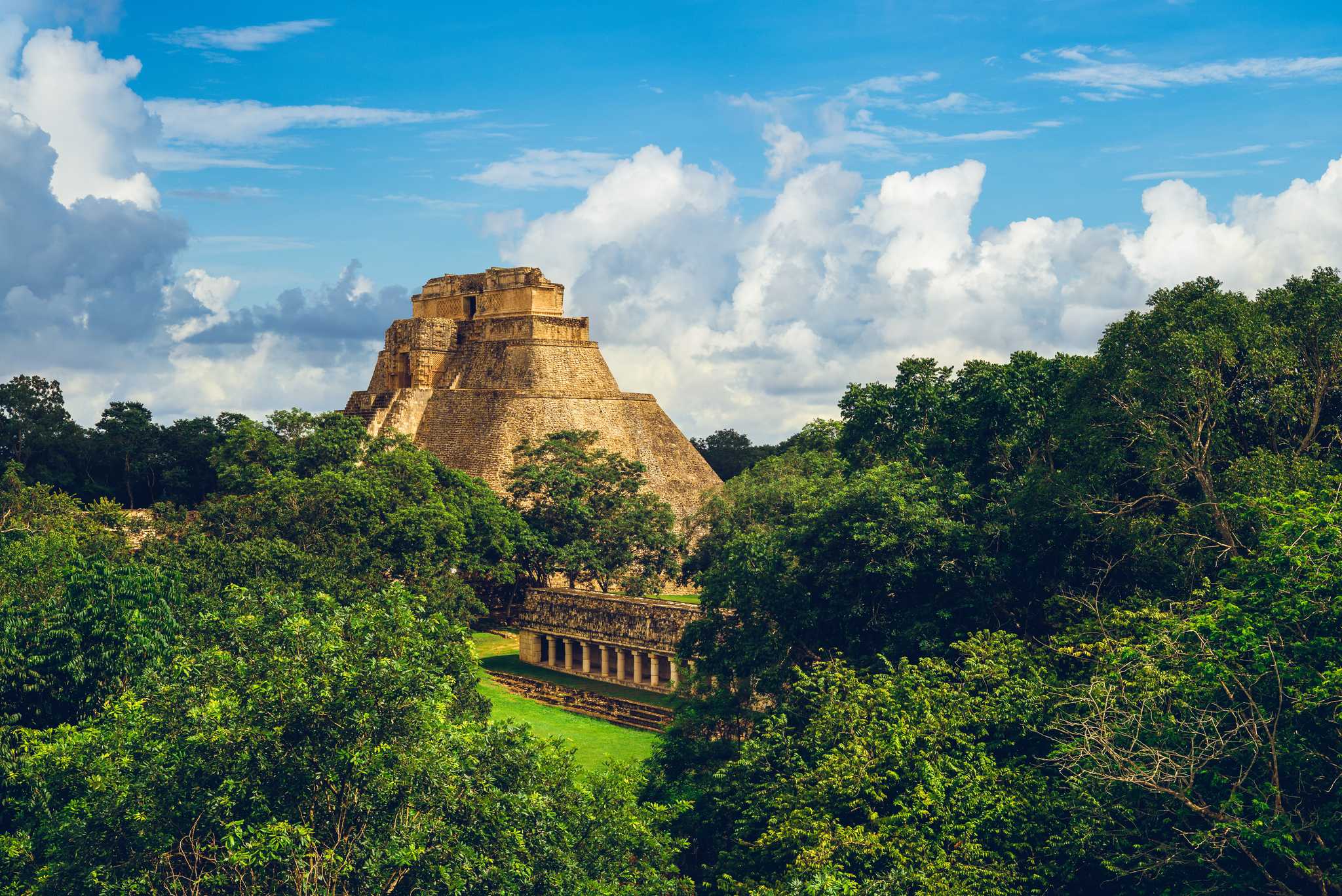 Pyramid of the Magician in Uxmal, peeking out behind lush green trees.