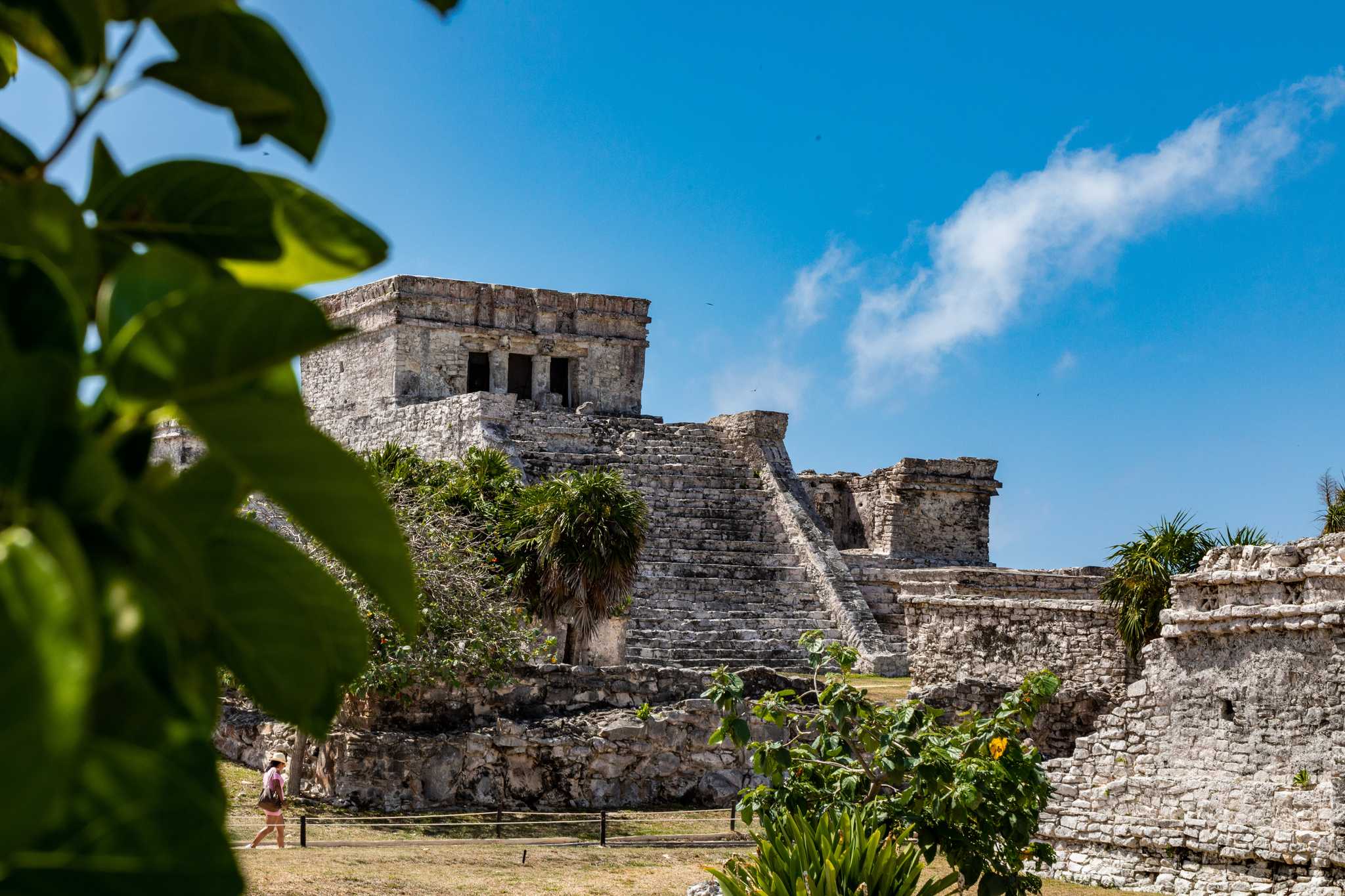 Stone temple in Tulum framed by tropical leaves under a blue sky.