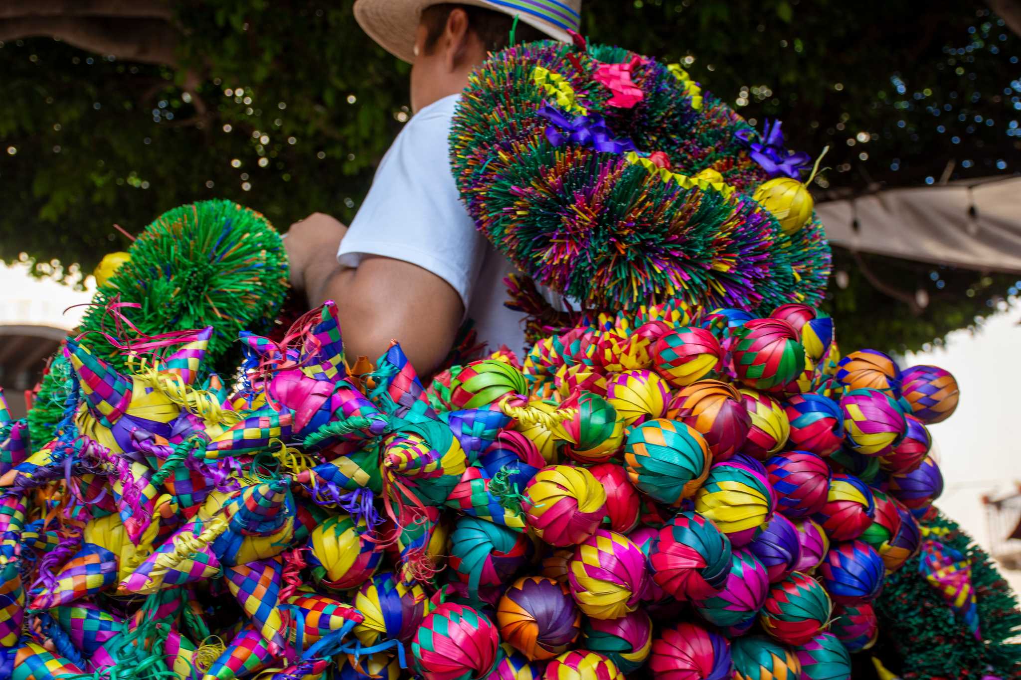 Vendor carries straw wreaths and colorful ornaments in a Mexican Christmas market.