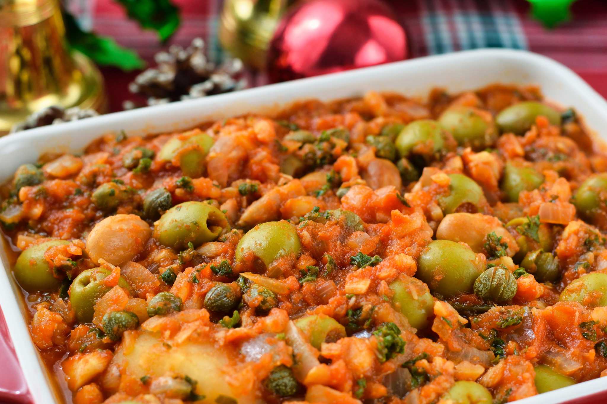 Close up of Bacalao a la Vizcaína with green olives and capers in a white dish.