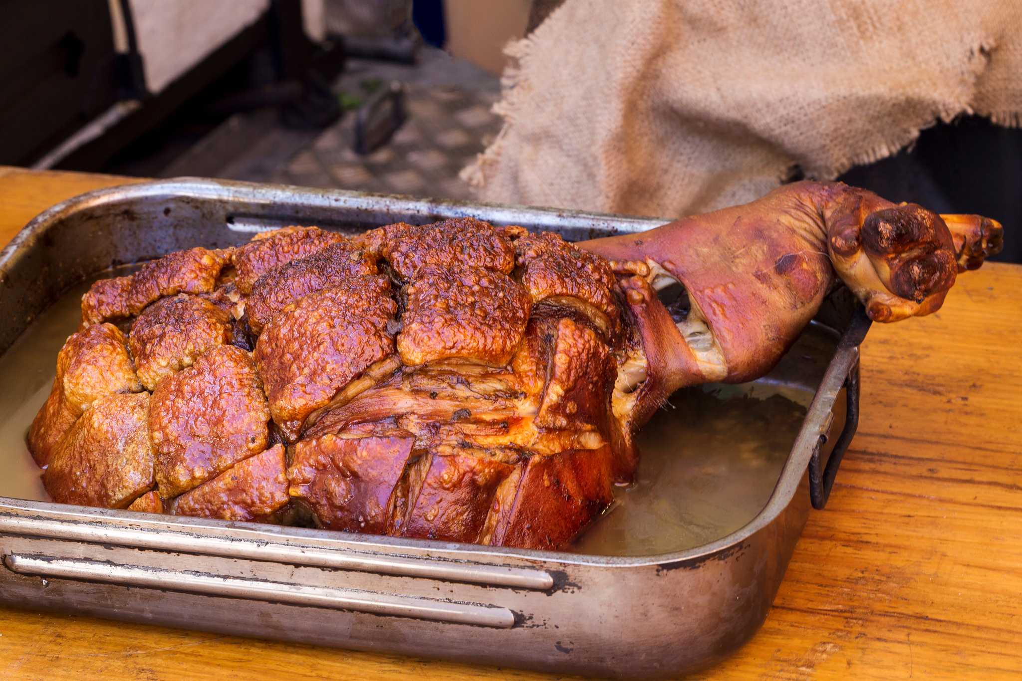 Roast pork left in a metal baking tray atop a wooden counter.