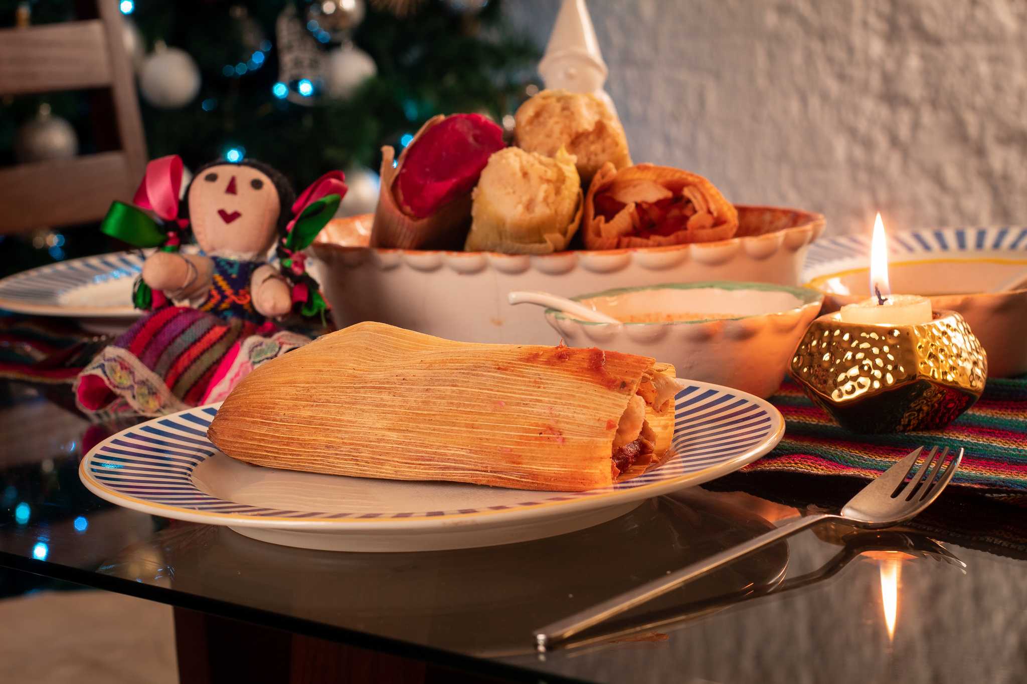 Mexican Tamales on a white plate with Christmas decorations and a candle behind.