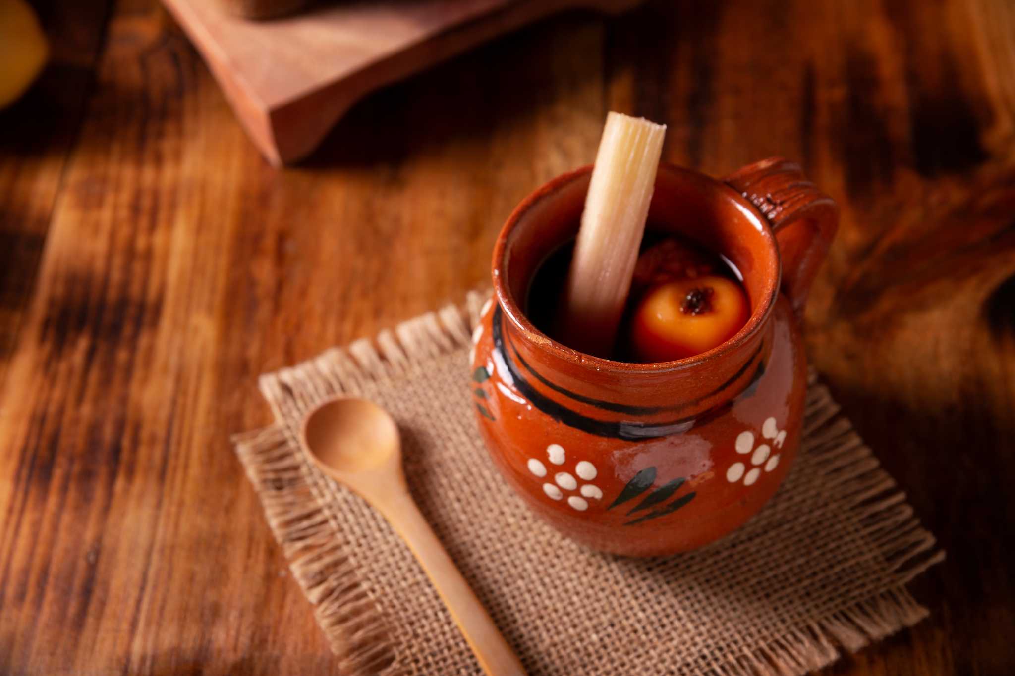 Decorated clay mug filled with ponche Navideno with sugarcane sticking out.