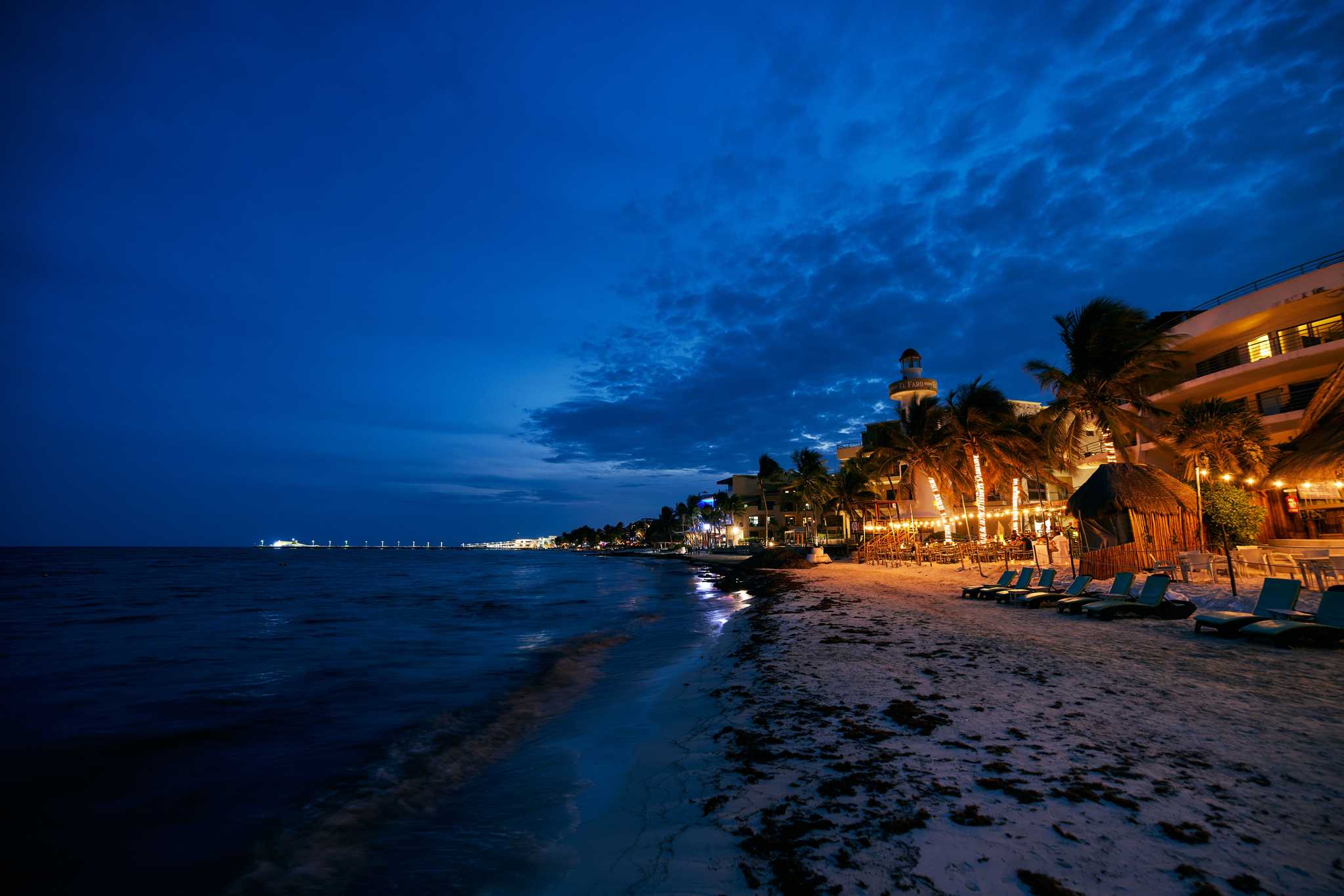 Playa del Carmen’s beach bars lit up at night, the ocean a dark blue on the left.