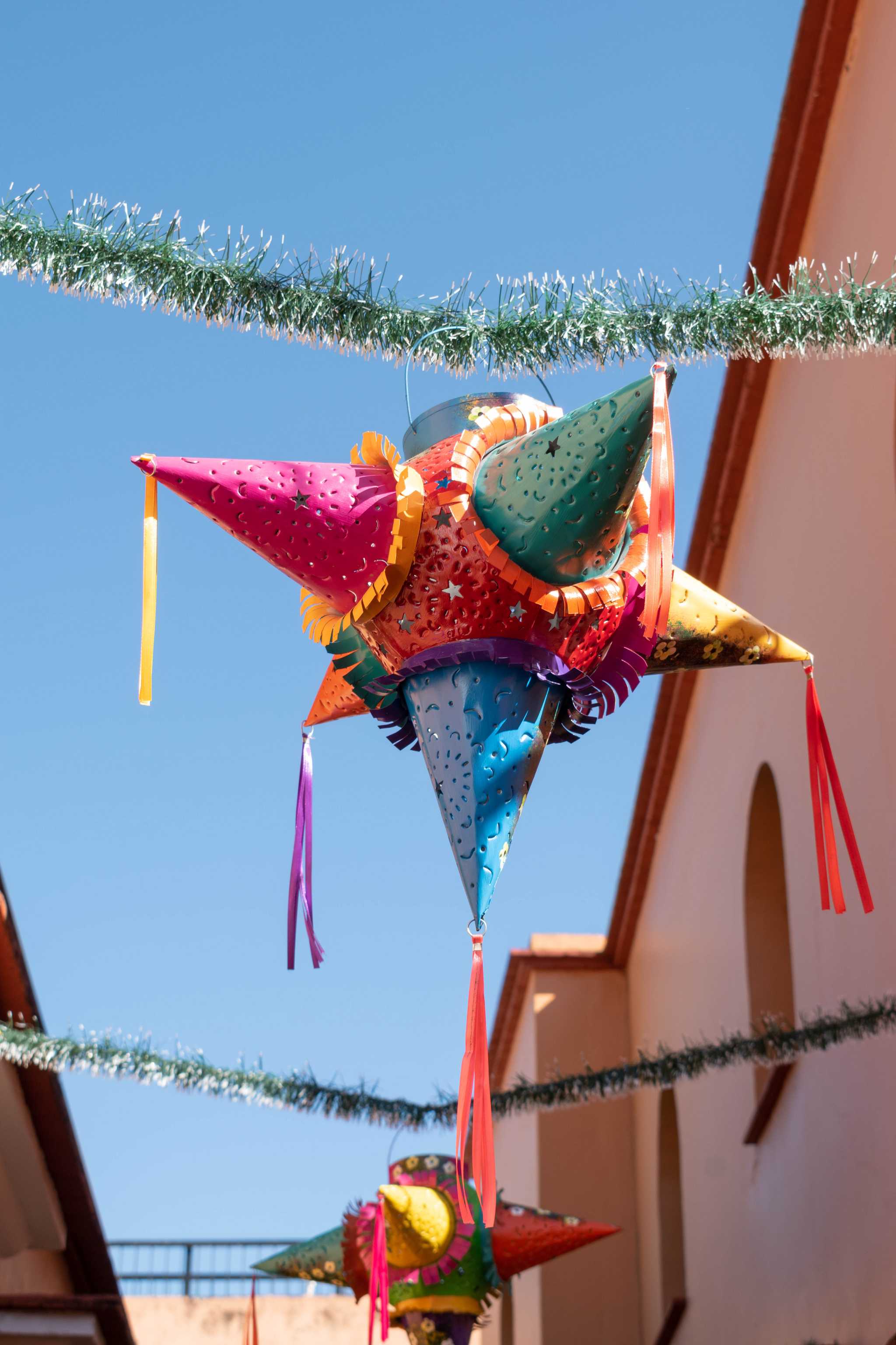 Colorful star pinata hanging on green Christmas garland in an alley in Mexico.