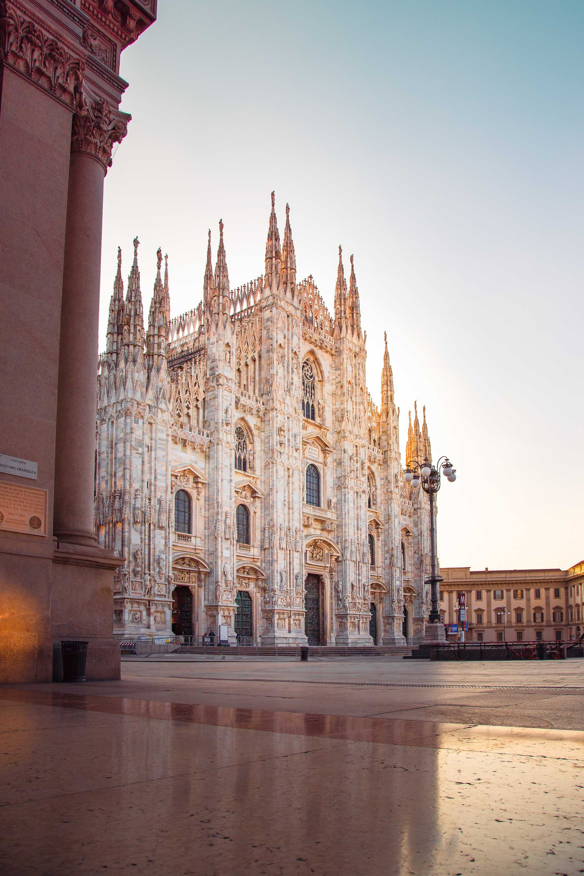 The white marble facade and spires of Milan's Duomo, seen across an empty Piazza del Duomo at dawn.